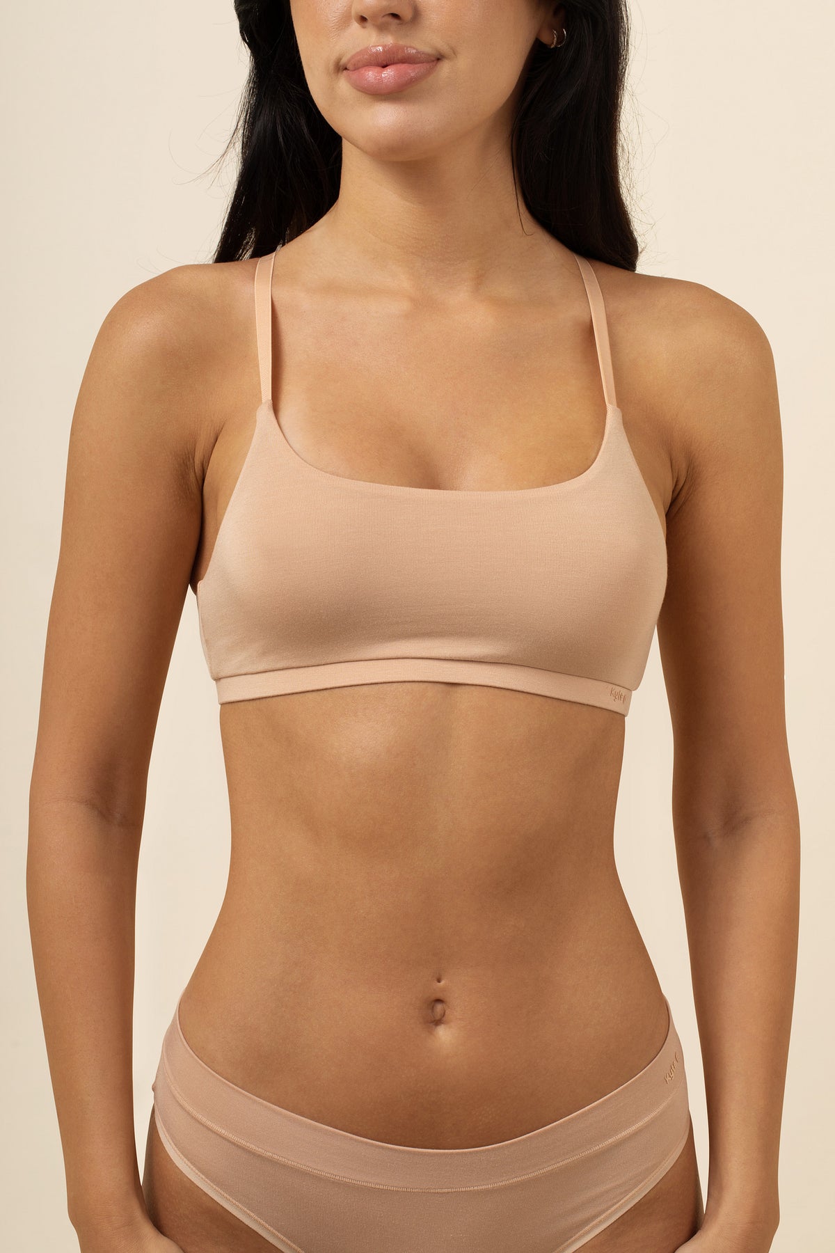 Woman wearing a beige bra and underwear set against a neutral background