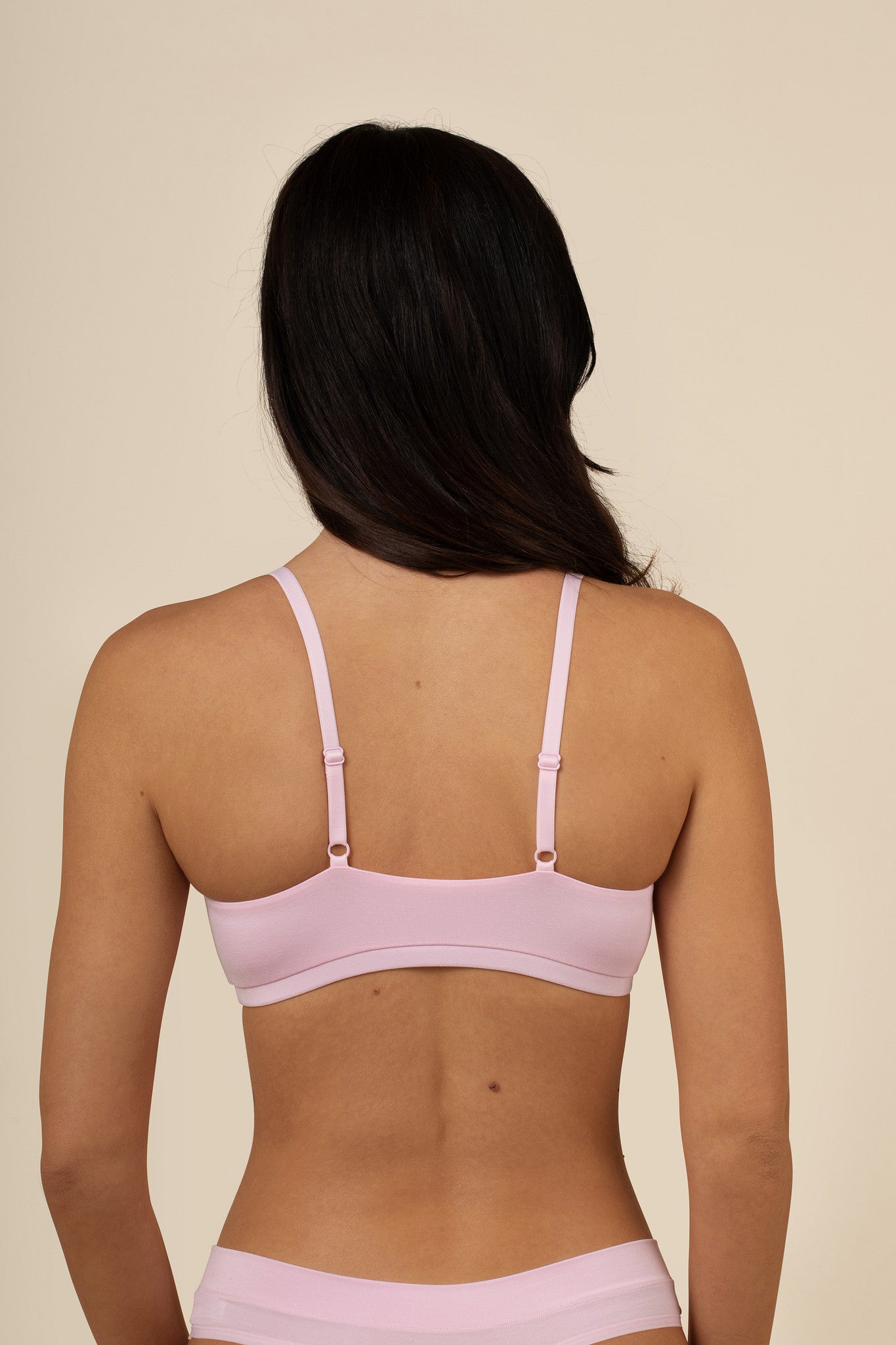 Woman wearing a pink scoop bra and underwear set against a beige background