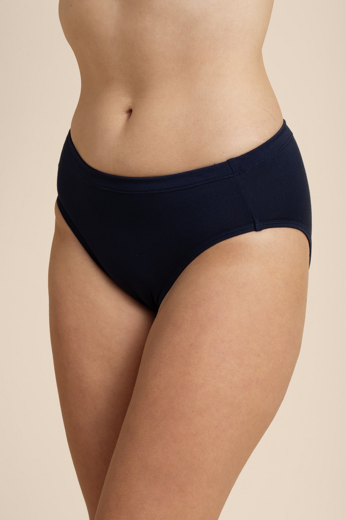Person wearing a navy bikini bottom on a beige background