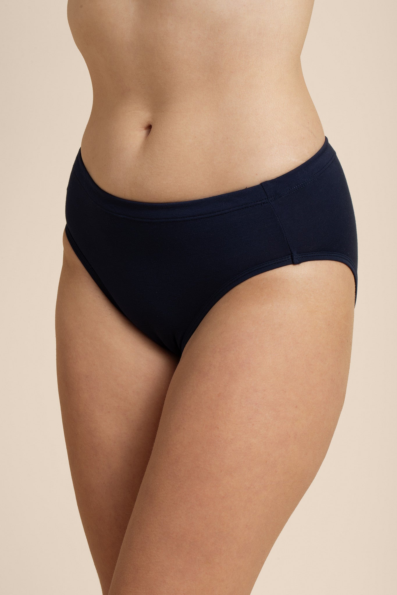 Person wearing a navy bikini bottom on a beige background