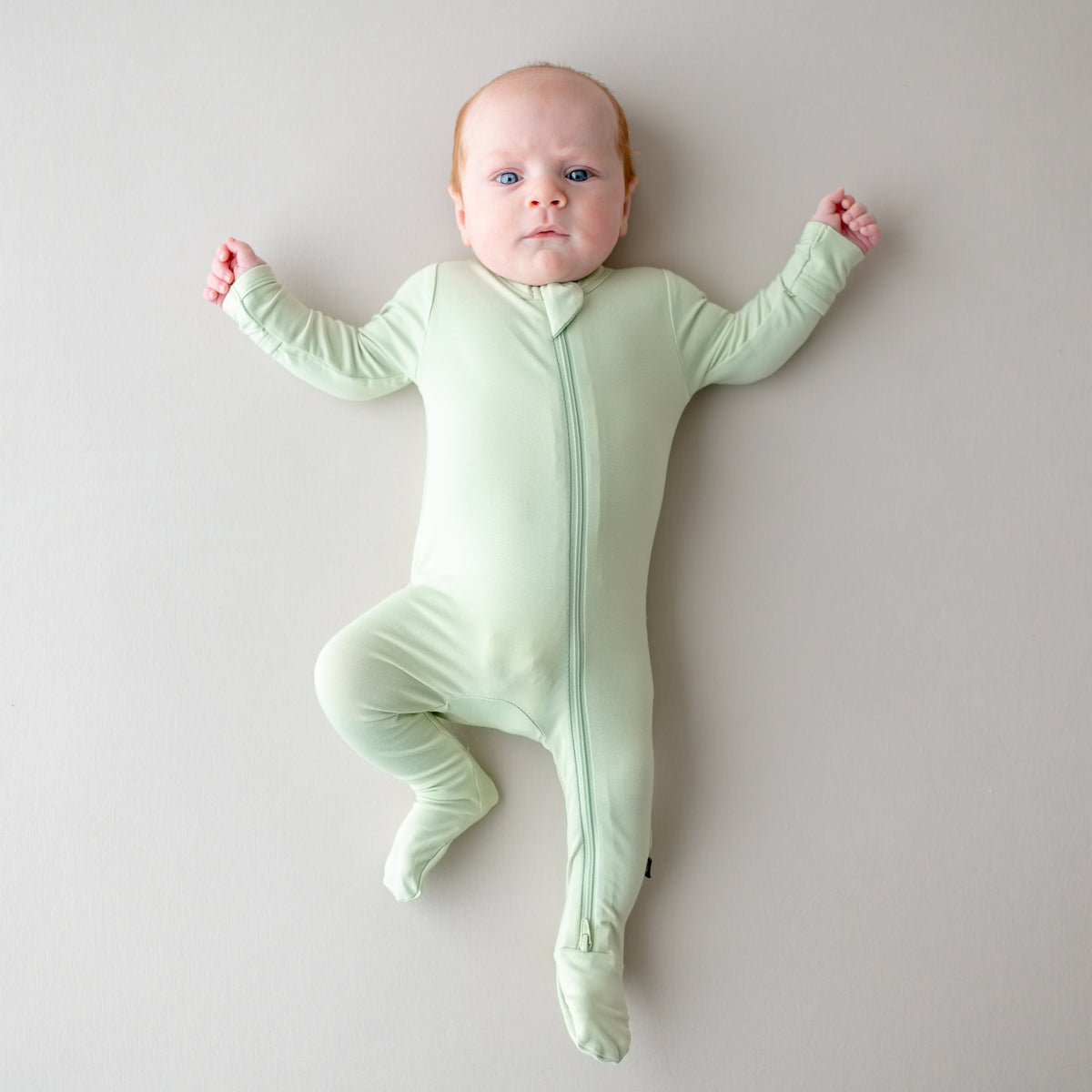 Baby wearing a light green zippered footie on a plain background