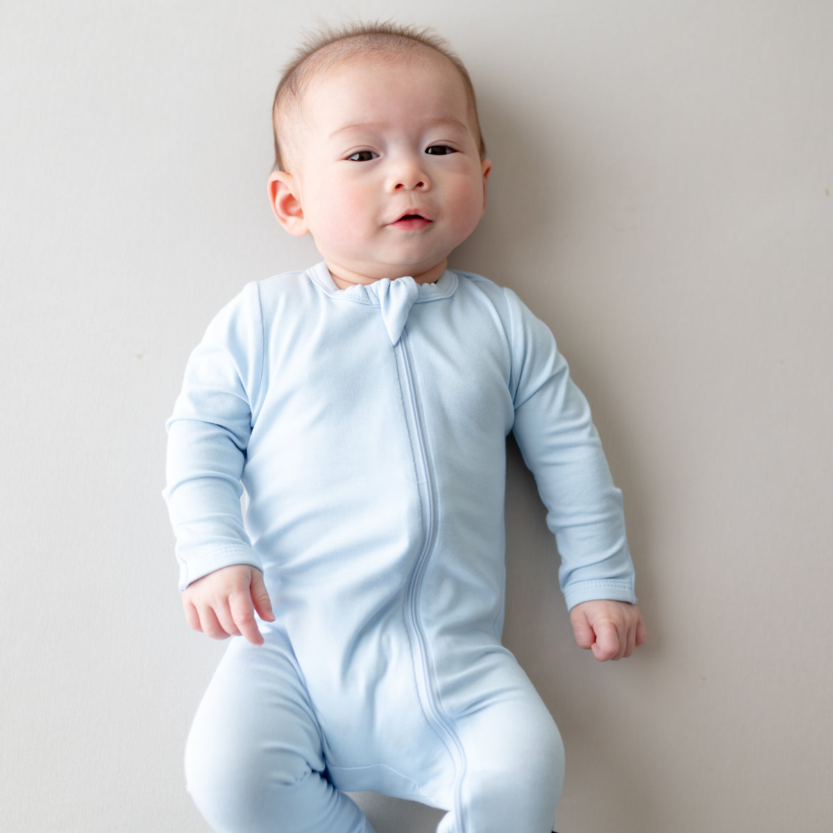 Baby wearing a light blue zippered footie against a plain background