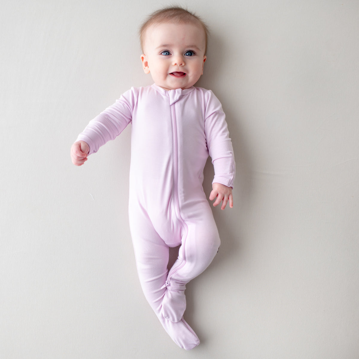 Baby smiling wearing a light purple zippered footie