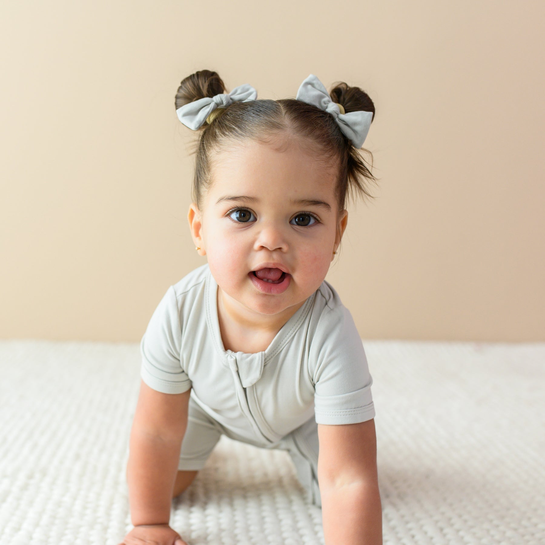 Toddler crawling towards camera while wearing Kyte Baby Zippered Shortall Romper in Oat 