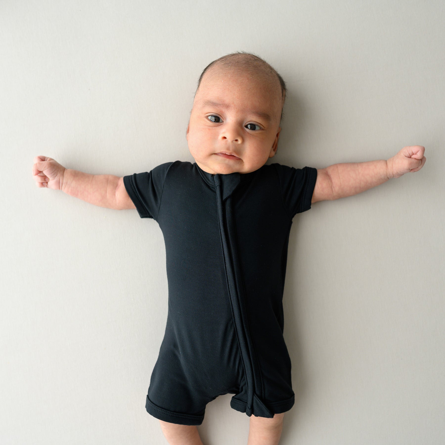 Infant lying on an oat surface while wearing a Zippered Shortall Romper in Midnight