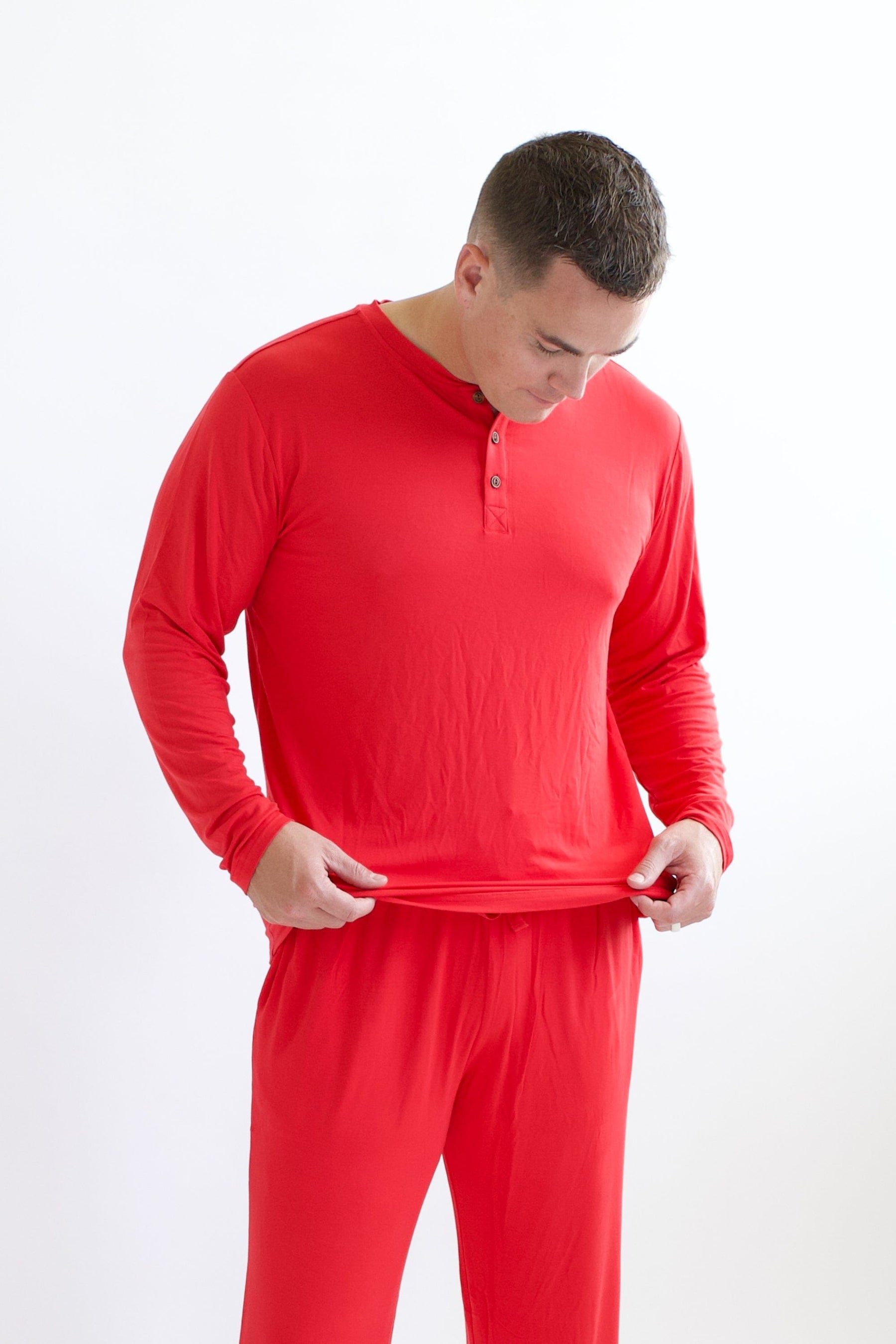 Male model  holding the bottom hem of the Men's Long Sleeve Henley Top in Cardinal in his hands standing in front of a white background