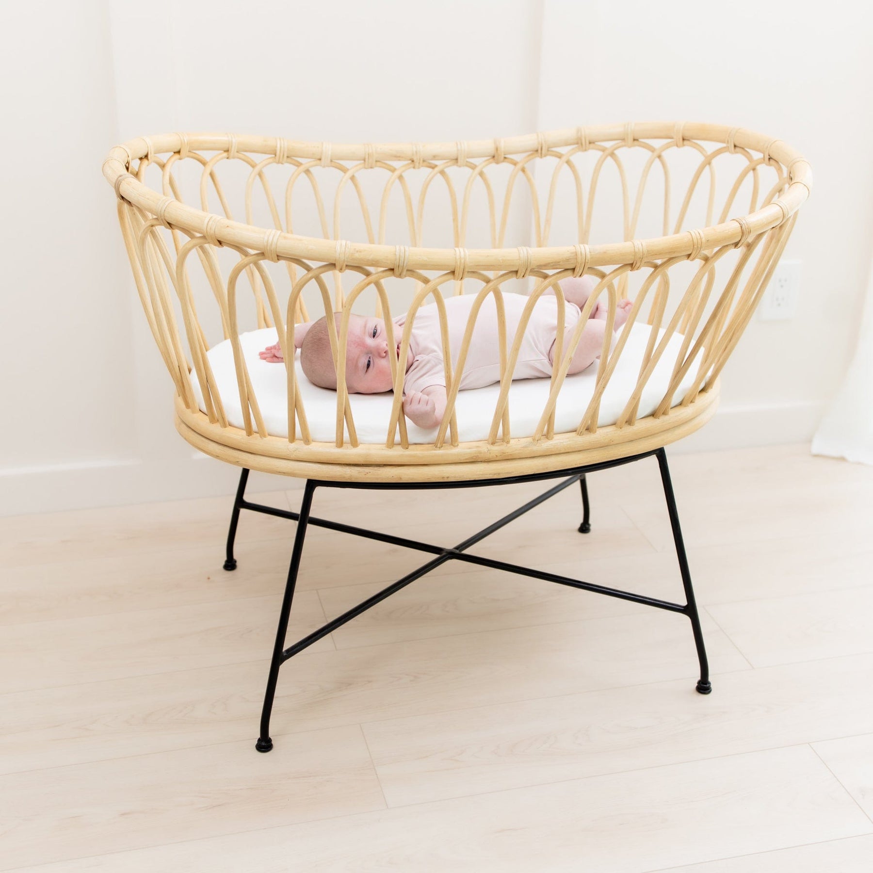 Baby laying on mattress covered with Kyte Baby Oval Bassinet Sheet in Cloud white