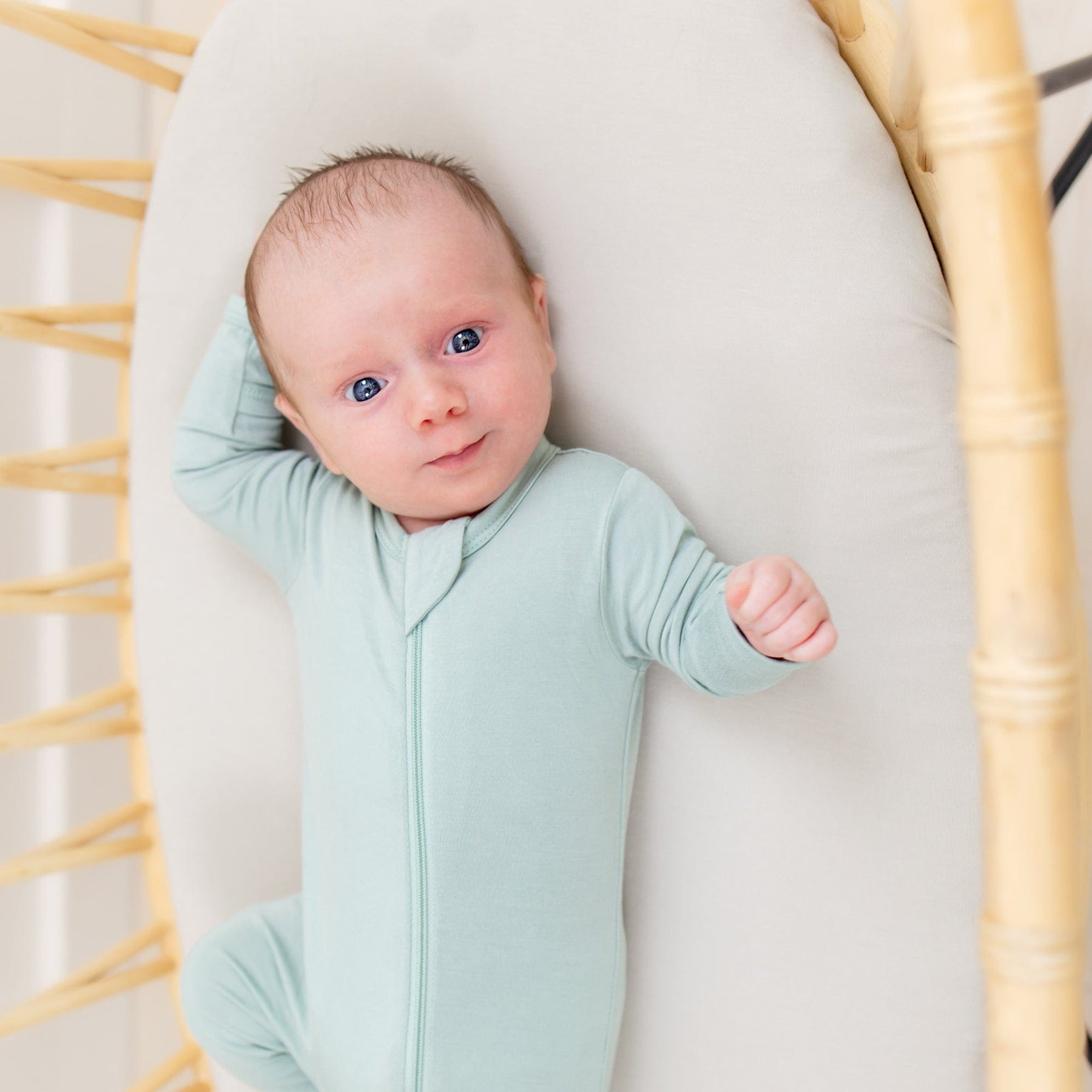 Infant laying on mattress covered with Kyte Baby Oval Bassinet Sheet in Oat