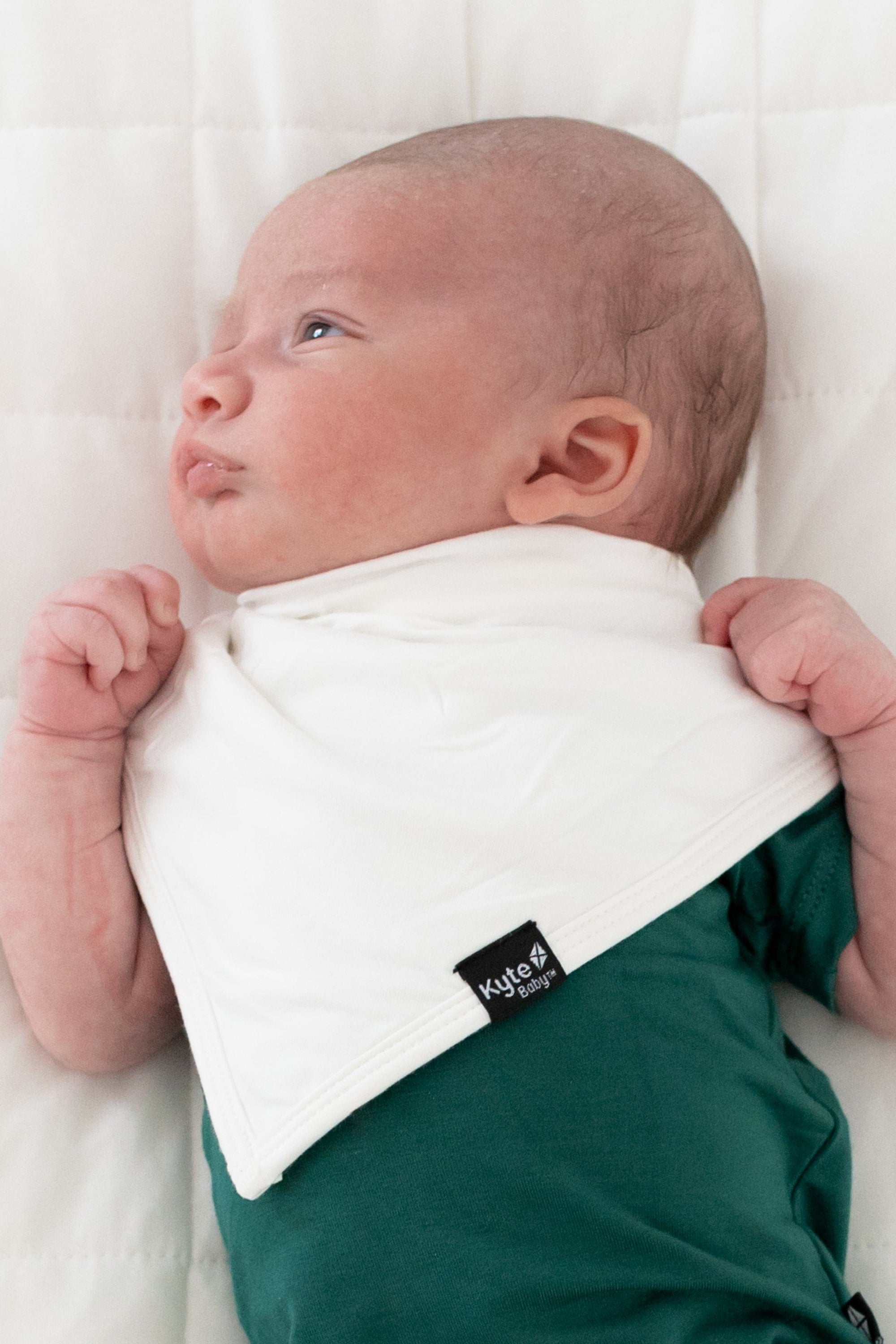 Infant wearing Kyte Baby Bib in Cloud and an Emerald Short sleeve bodysuit