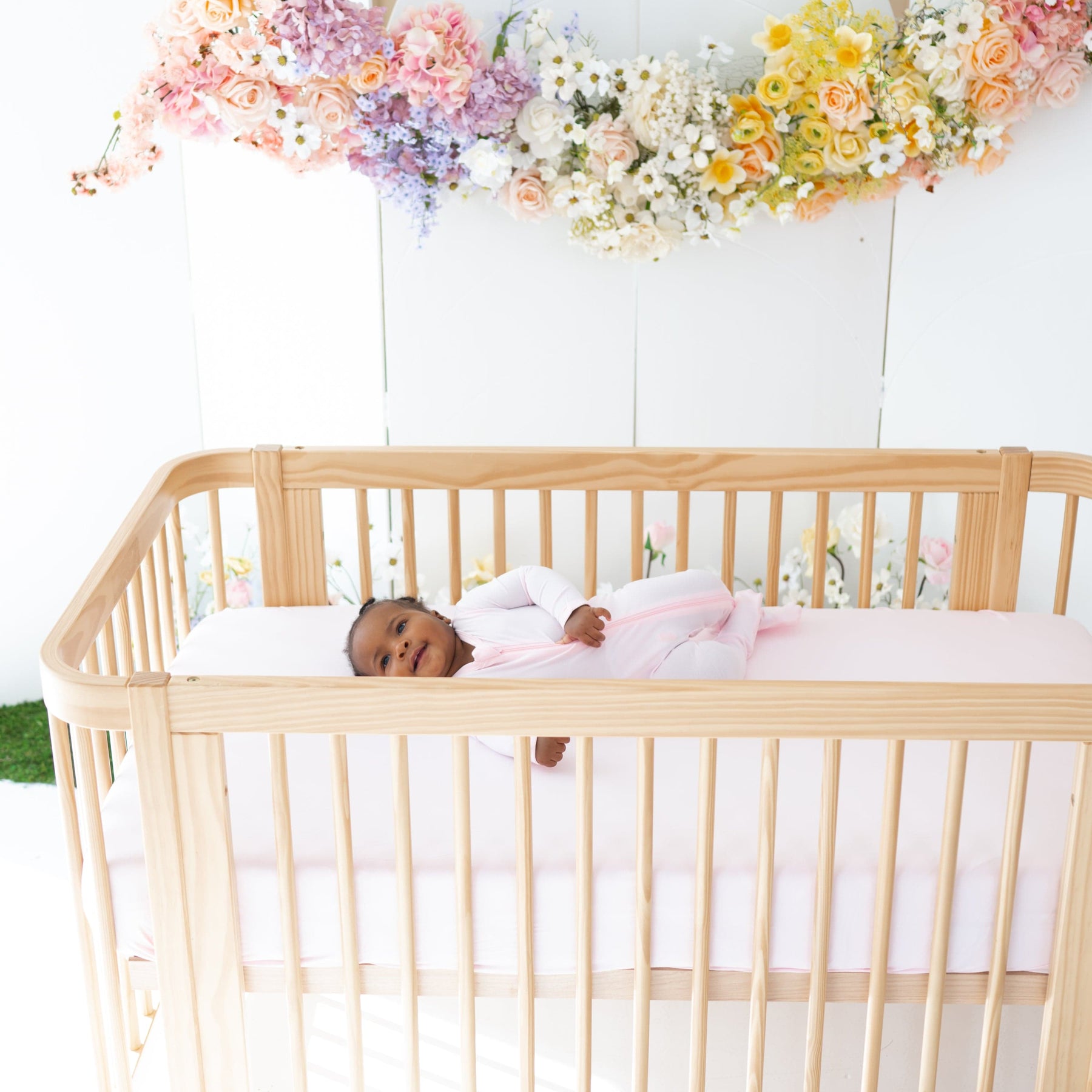 Infant laying on Kyte Baby Crib Sheet in Sakura pink