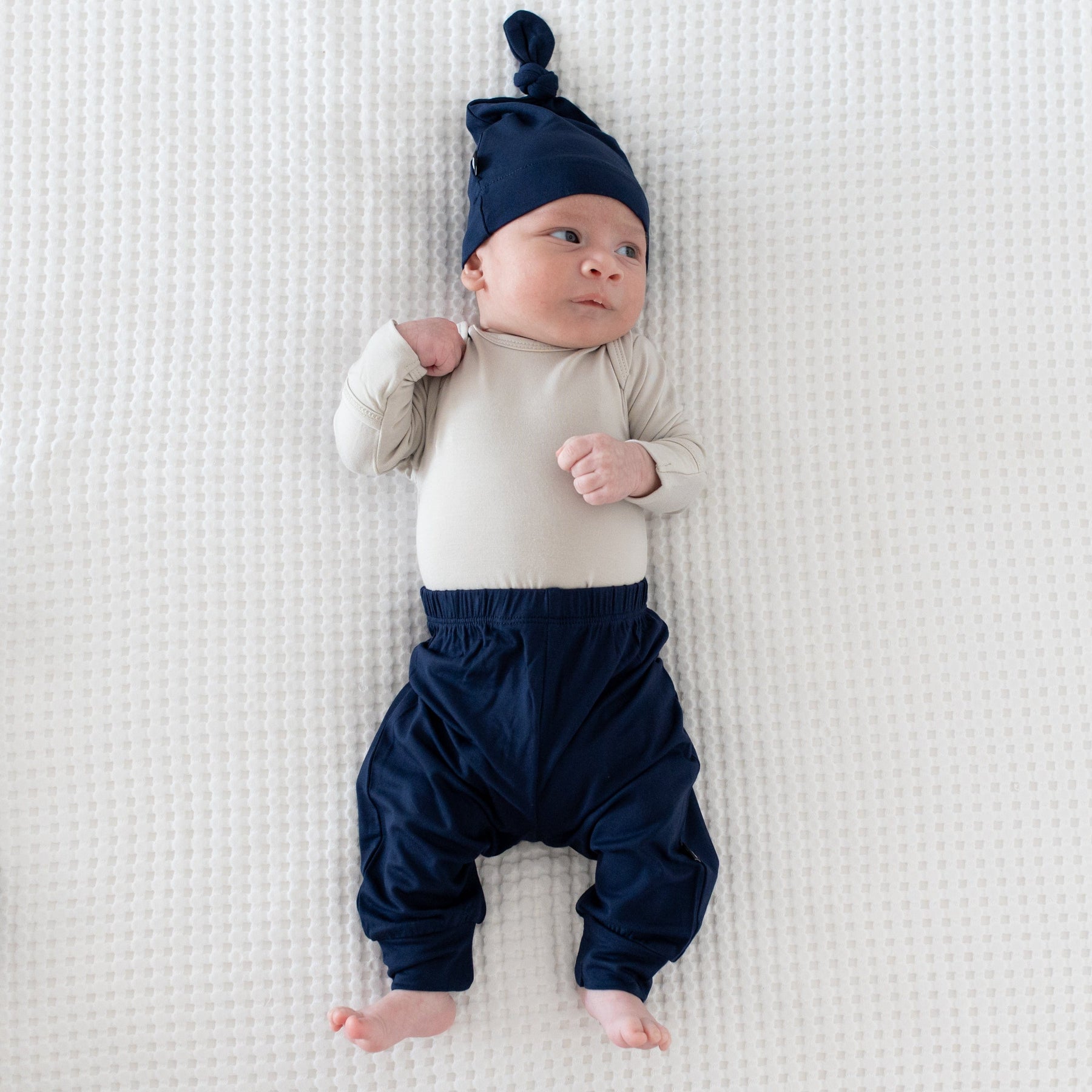 Newborn wearing Kyte Baby Knotted Cap in Navy with matching pants and a Long Sleeve Bodysuit in Oat