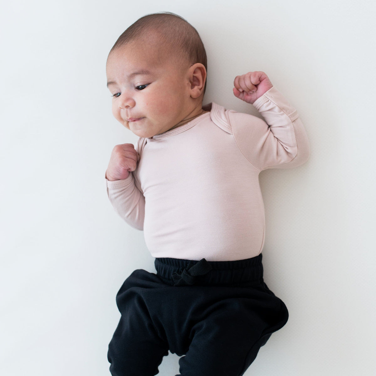 Newborn wearing Kyte Baby Long Sleeve Bodysuit in Blush with Pants in Midnight