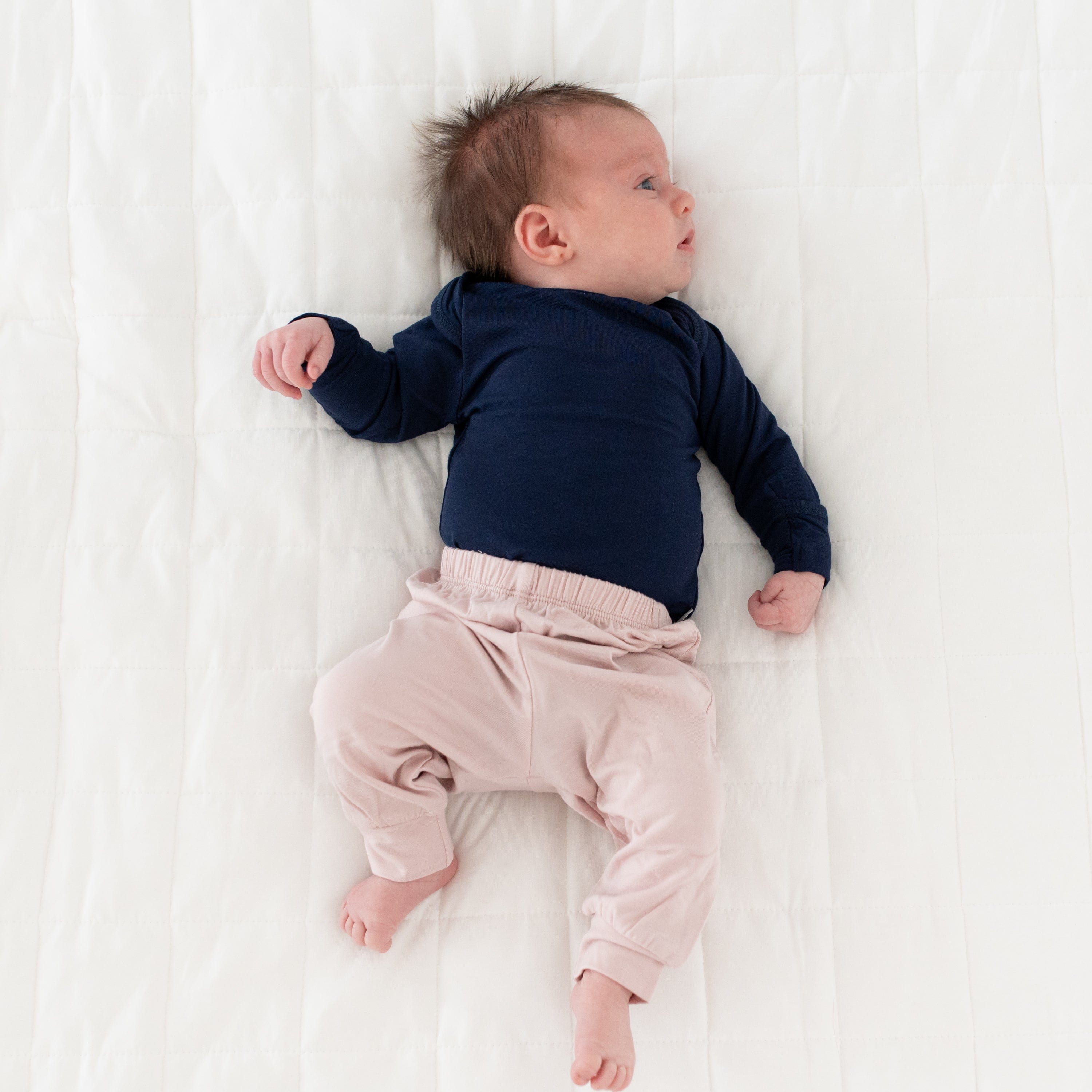 Newborn wearing Kyte Baby Pants in Blush and Long Sleeve Bodysuit in Navy