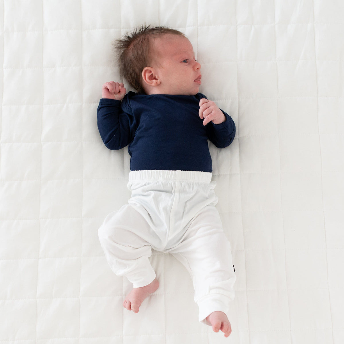 Newborn laying on white background wearing Kyte Baby Pant in Cloud with Navy Long Sleeve Bodysuit. 