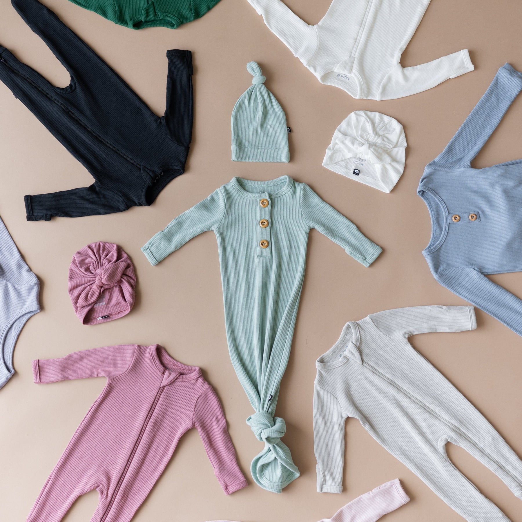 Kyte Baby Ribbed pajamas and headwraps in multiple colors on a light brown surface