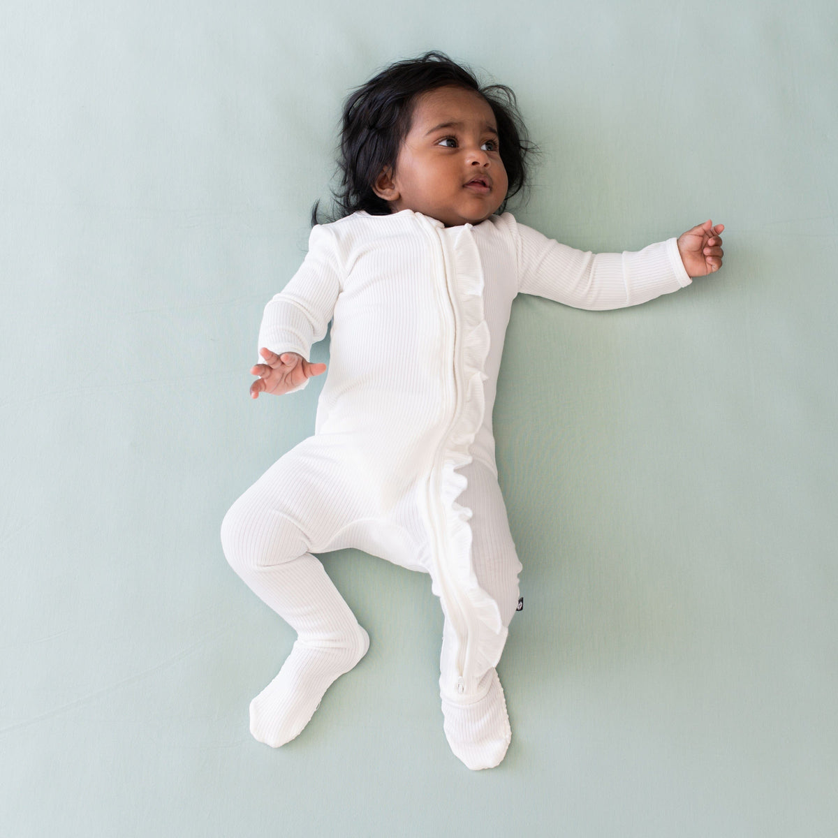 Infant wearing Kyte Baby Ribbed Ruffle Zipper Footie in Cloud