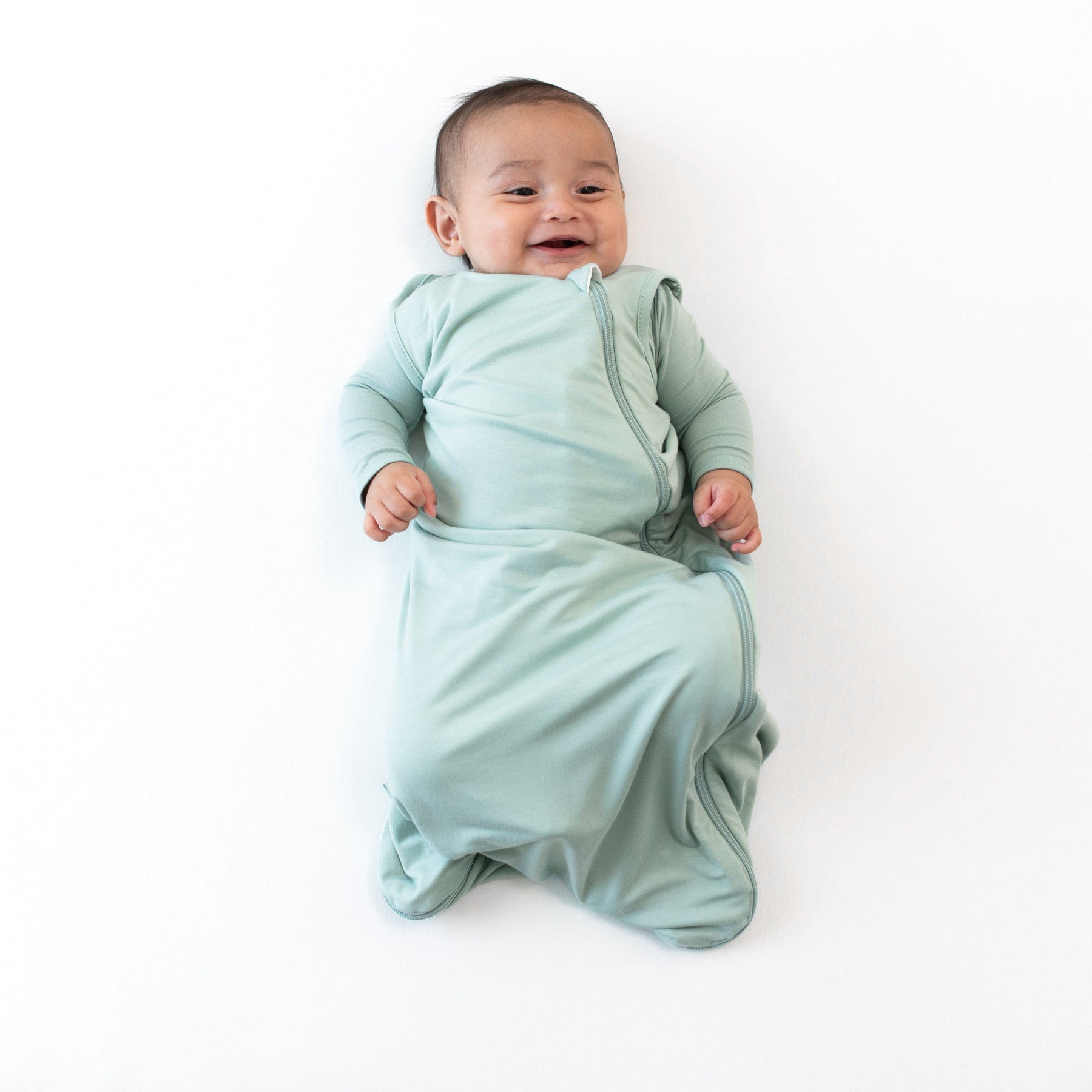 Smiling infant wearing the  0.5 Tog Sleep Bag in Sage with a Sage long sleeve romper underneath