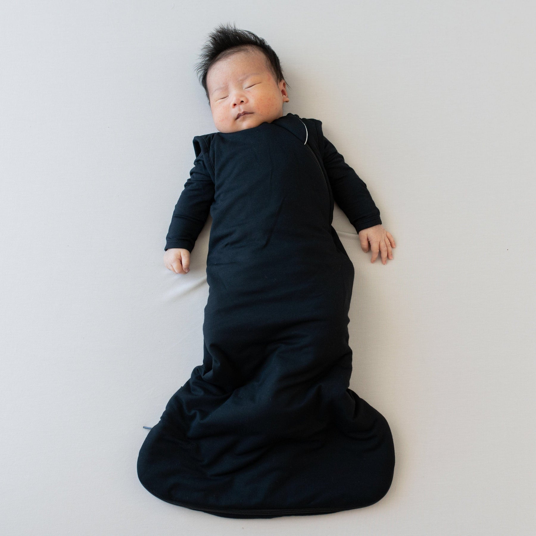 Sleeping infant in Kyte Baby Sleep Bag in Midnight 1.0 and a matching long sleeve bodysuit underneath 