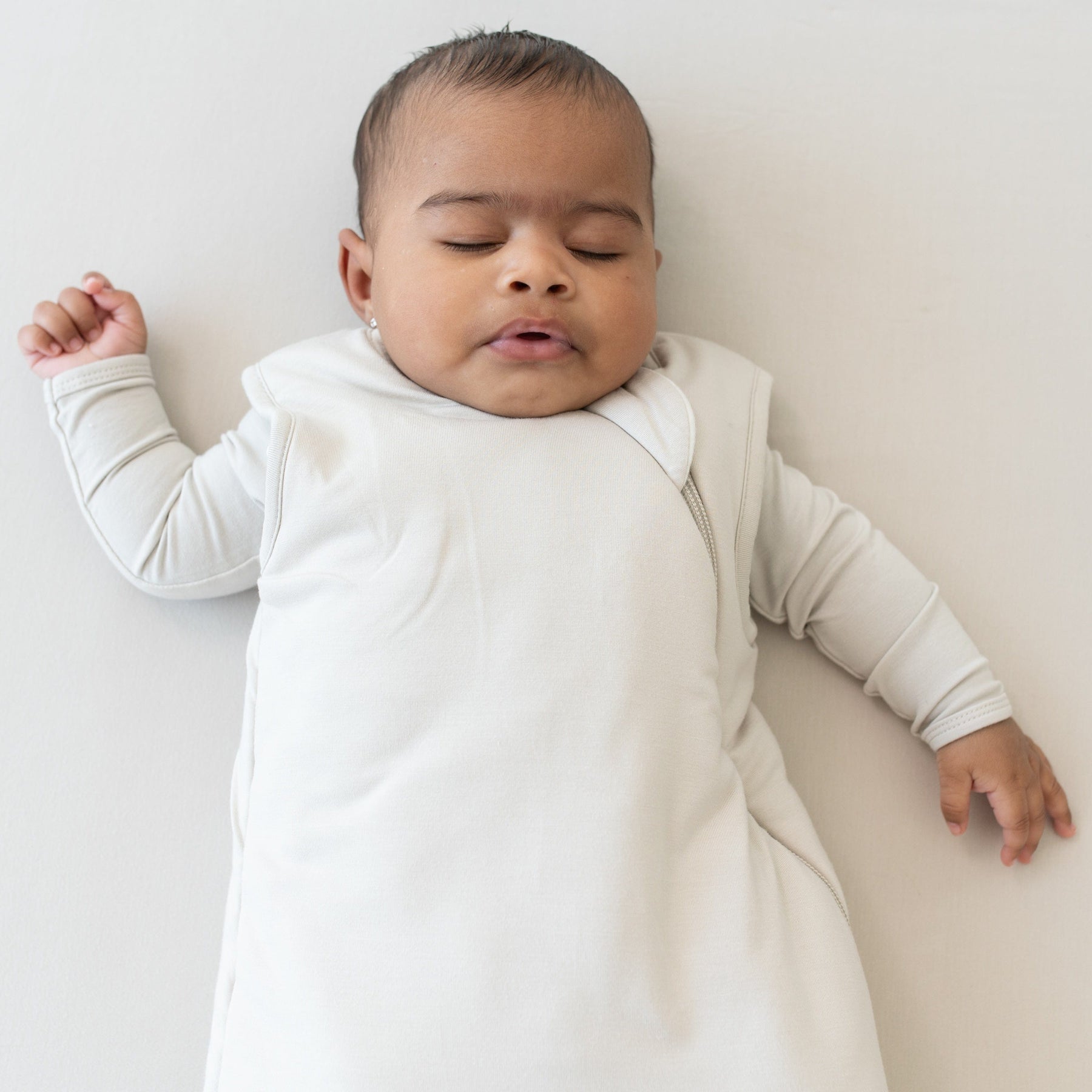 Close up of  baby sleeping on an Oat surface while wearing the Sleep Bag in Oat  2.5 