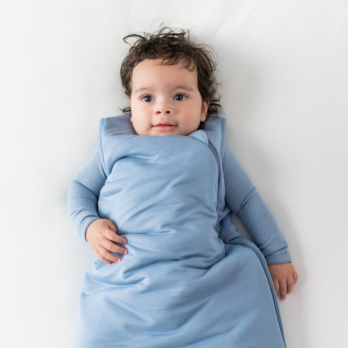 Baby laying on its back on an off white surface and wearing a Sleep Bag in Slate in 2.5 TOG 