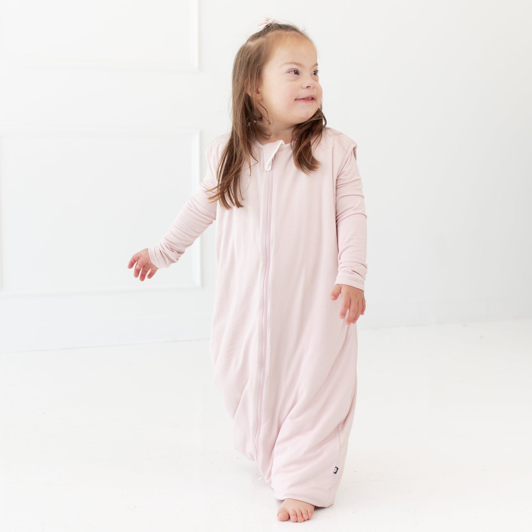Standing toddler looking to the right hand side while wearing a Kyte Baby Sleep Bag Walker 1.0  in Blush