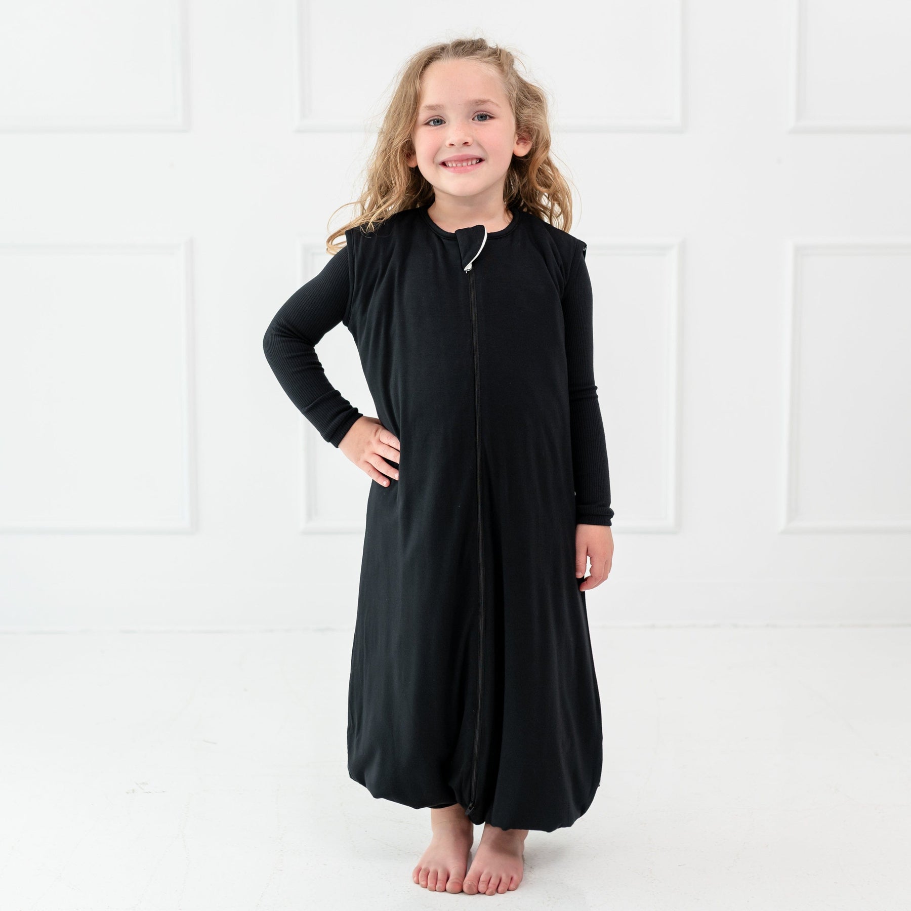 Girl model standing infront of whilte wall while wearing Sleep Bag Walker in Midnight 1.0 with one hand on her waist