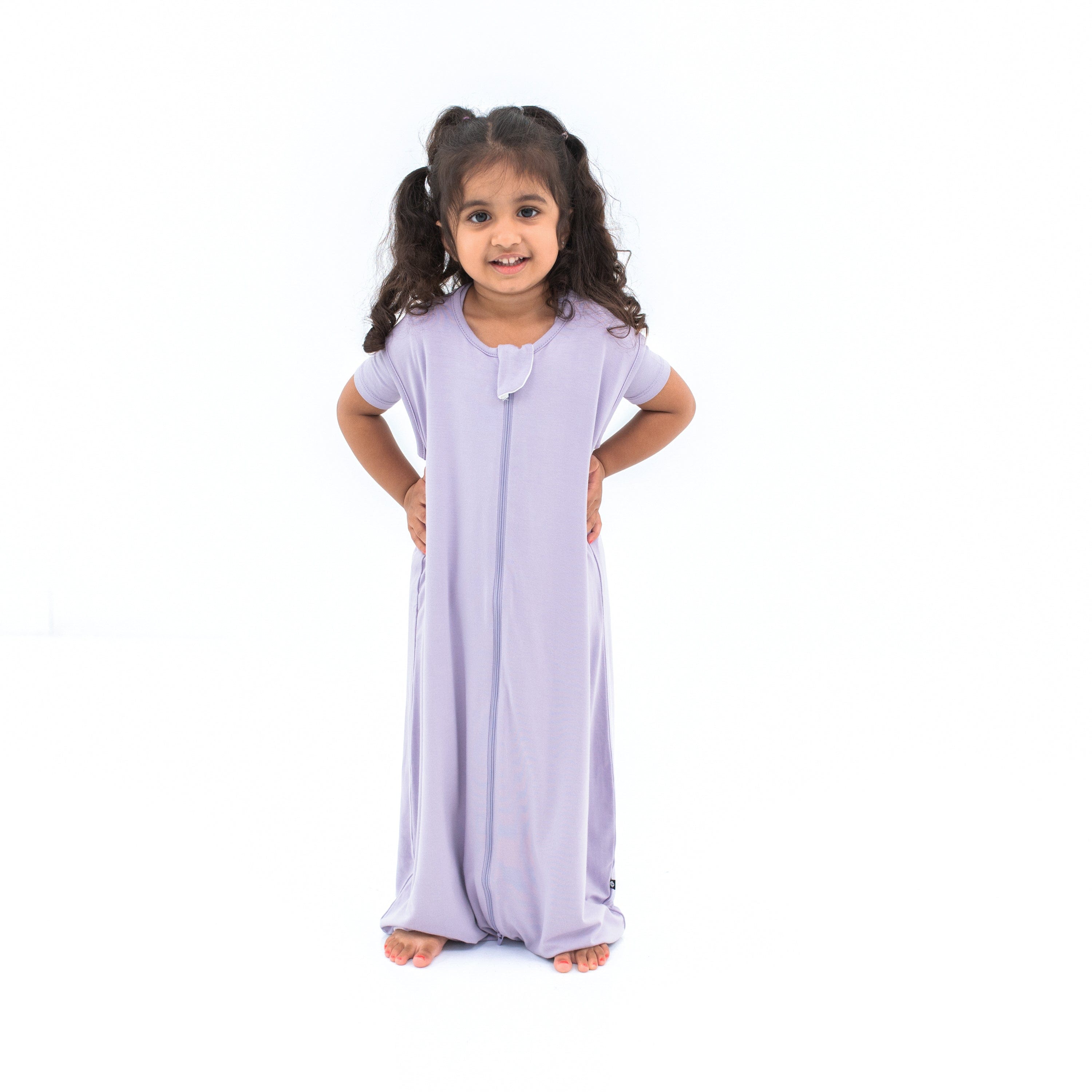Girl model wearing the Sleep Bag Walker in Taro 0.5 with both hands on her hips