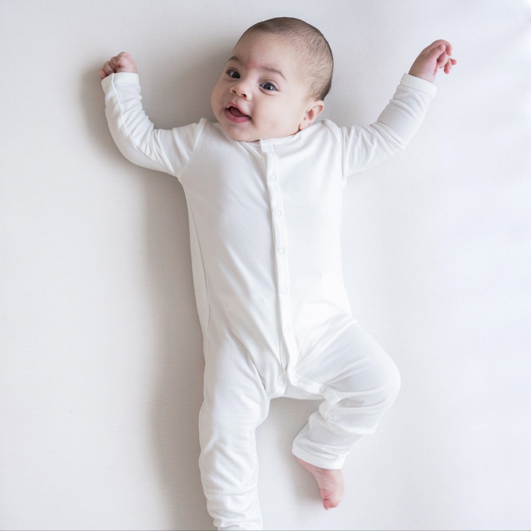 Infant laying on white background wearing Kyte Baby Snap Romper Romper in Cloud