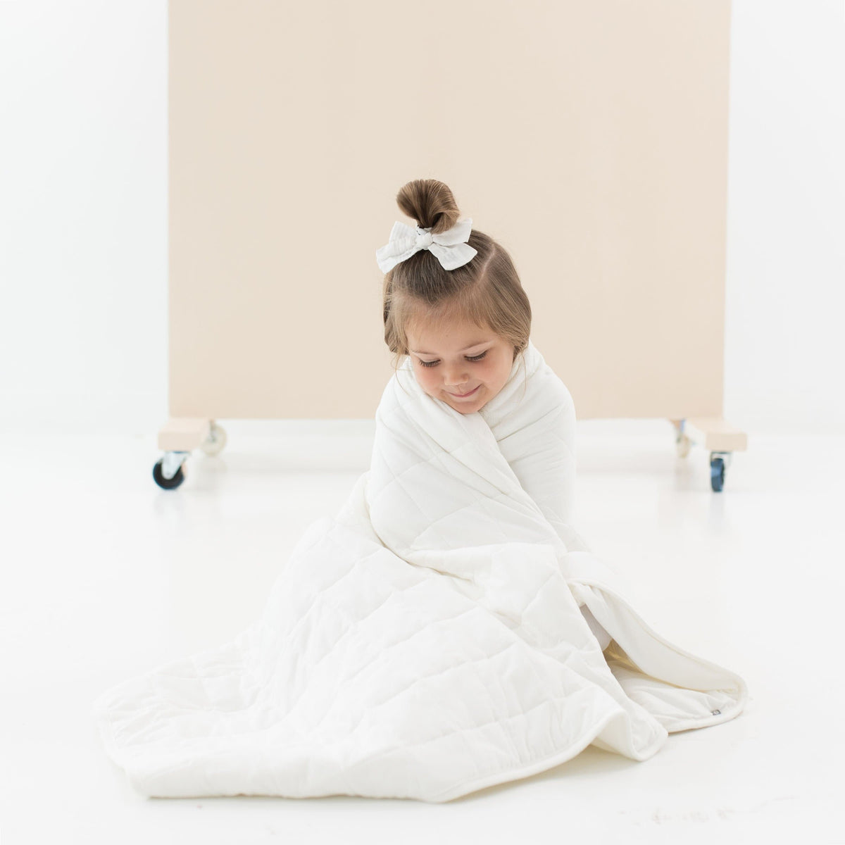 Child sitting on the floor wrapped in Kyte Baby TOG 2.5 Toddler Blanket in Cloud 