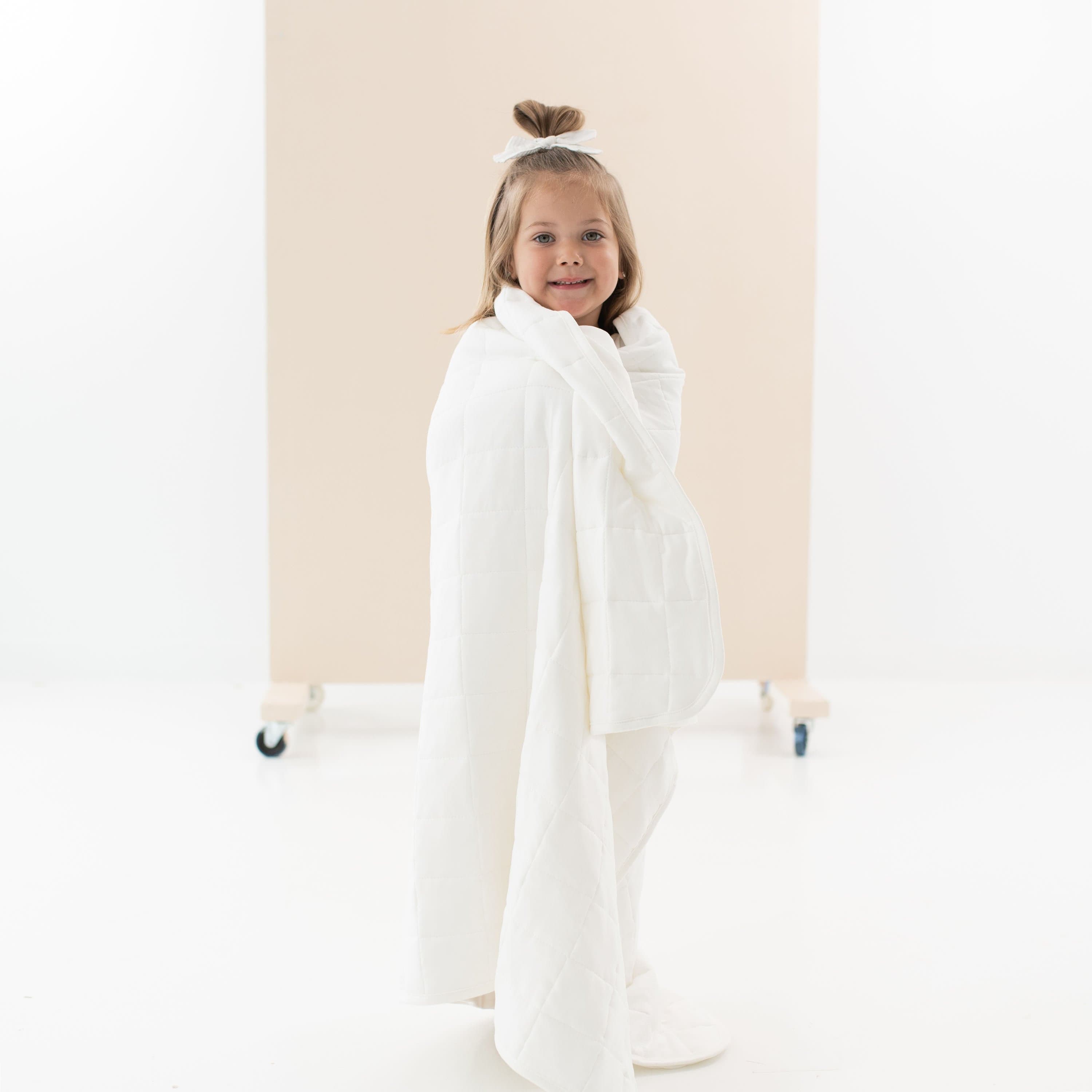 Child standing while wrapped in Kyte Baby Toddler Blanket in Cloud 2.5