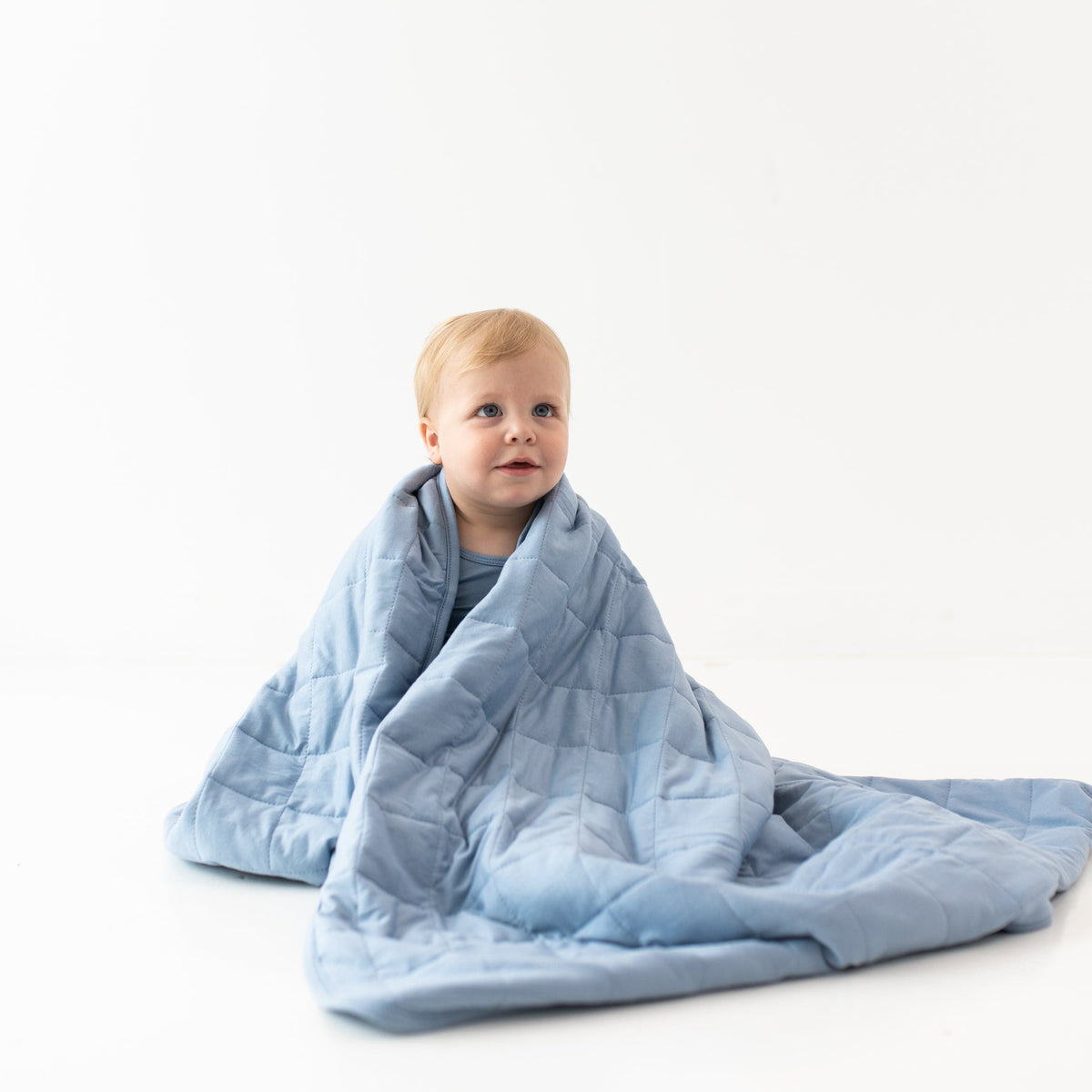 Child sitting in a white room wrapped in a Toddler Blanket in Slate 2.5 TOG