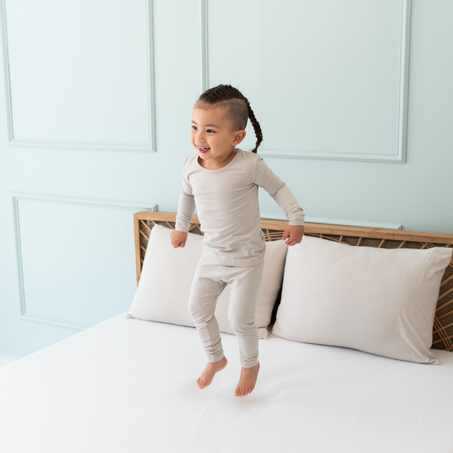 Toddler jumping in a bed while wearing Long Sleeve Kids Pajamas in Oat