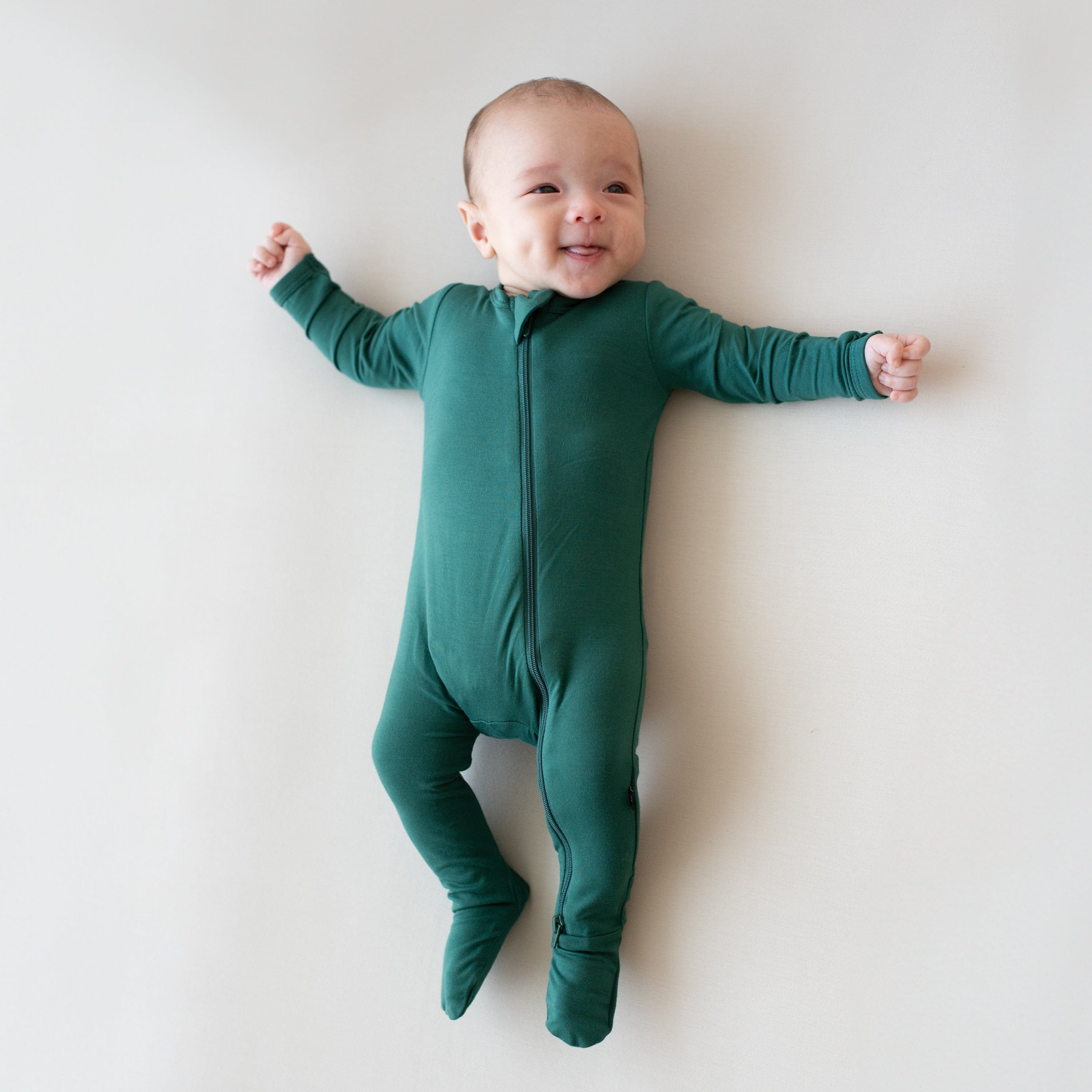 Baby laying on an oat surface and wearing Zippered Footie in Emerald