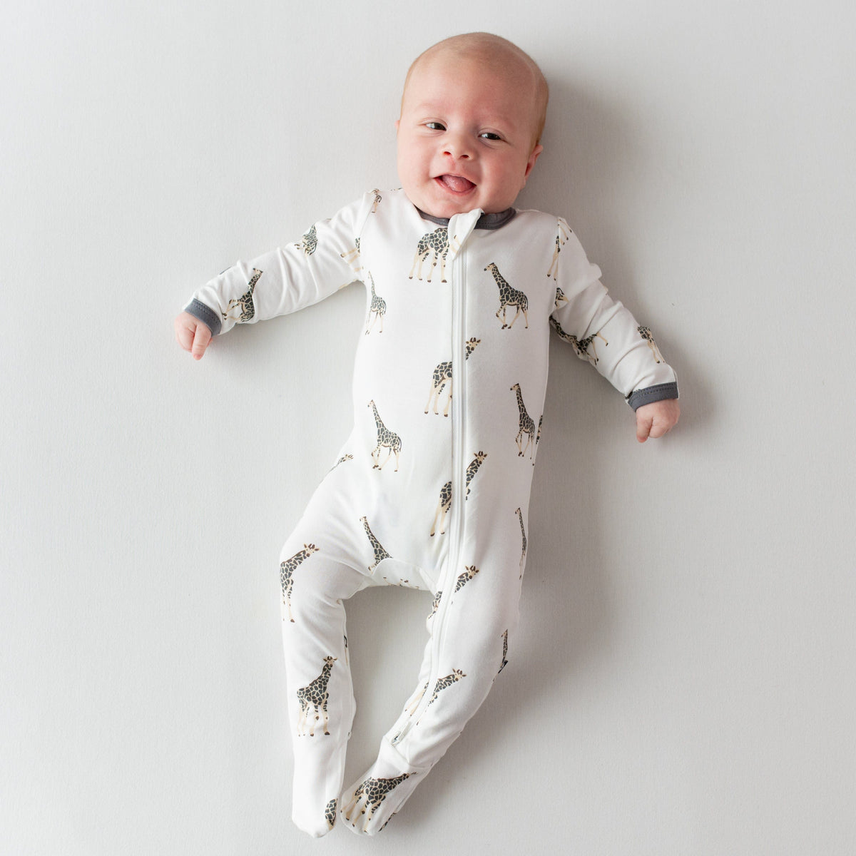 Infant sticking tongue out wearing Kyte Baby Zippered Footie in Giraffe