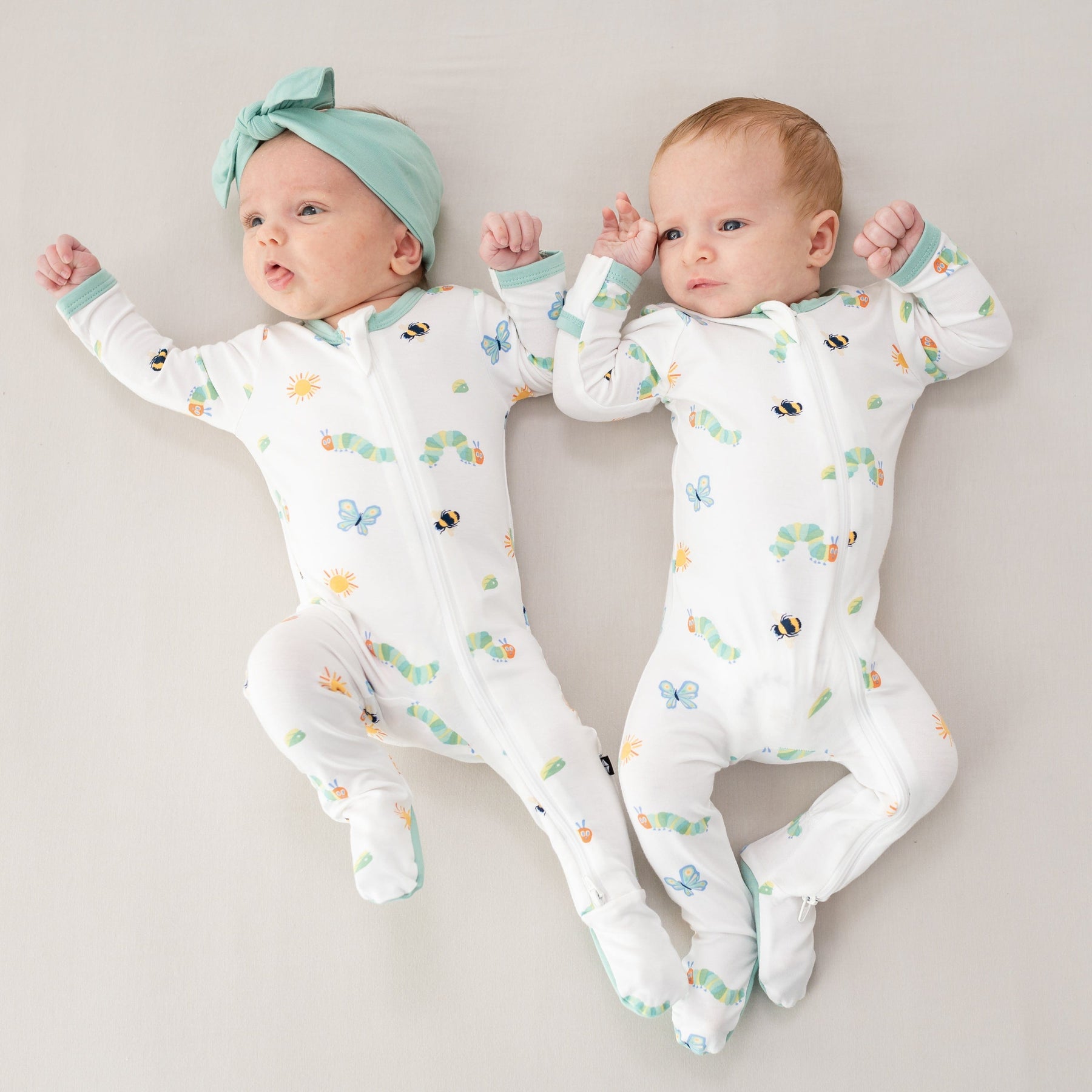 Two infants lying side by side both wearing the Zippered Footie in The Very Hungry Caterpillar™ and Friends