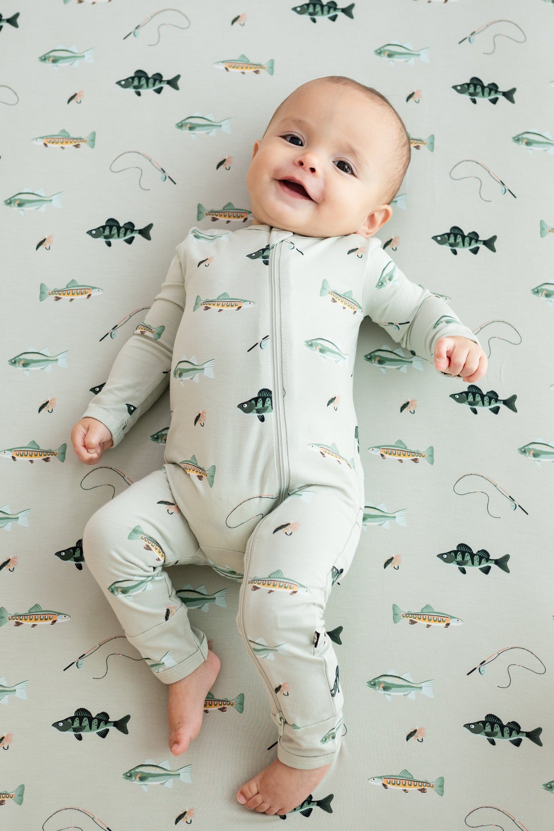 Infant model wearing the Zippered Romper in Fishing laying on a Fishing Crib Sheet