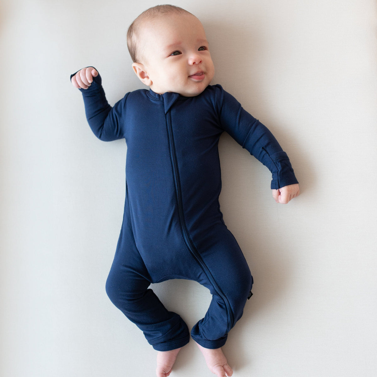 Infant laying on an Oat surface while wearing a  Zippered Romper in Navy