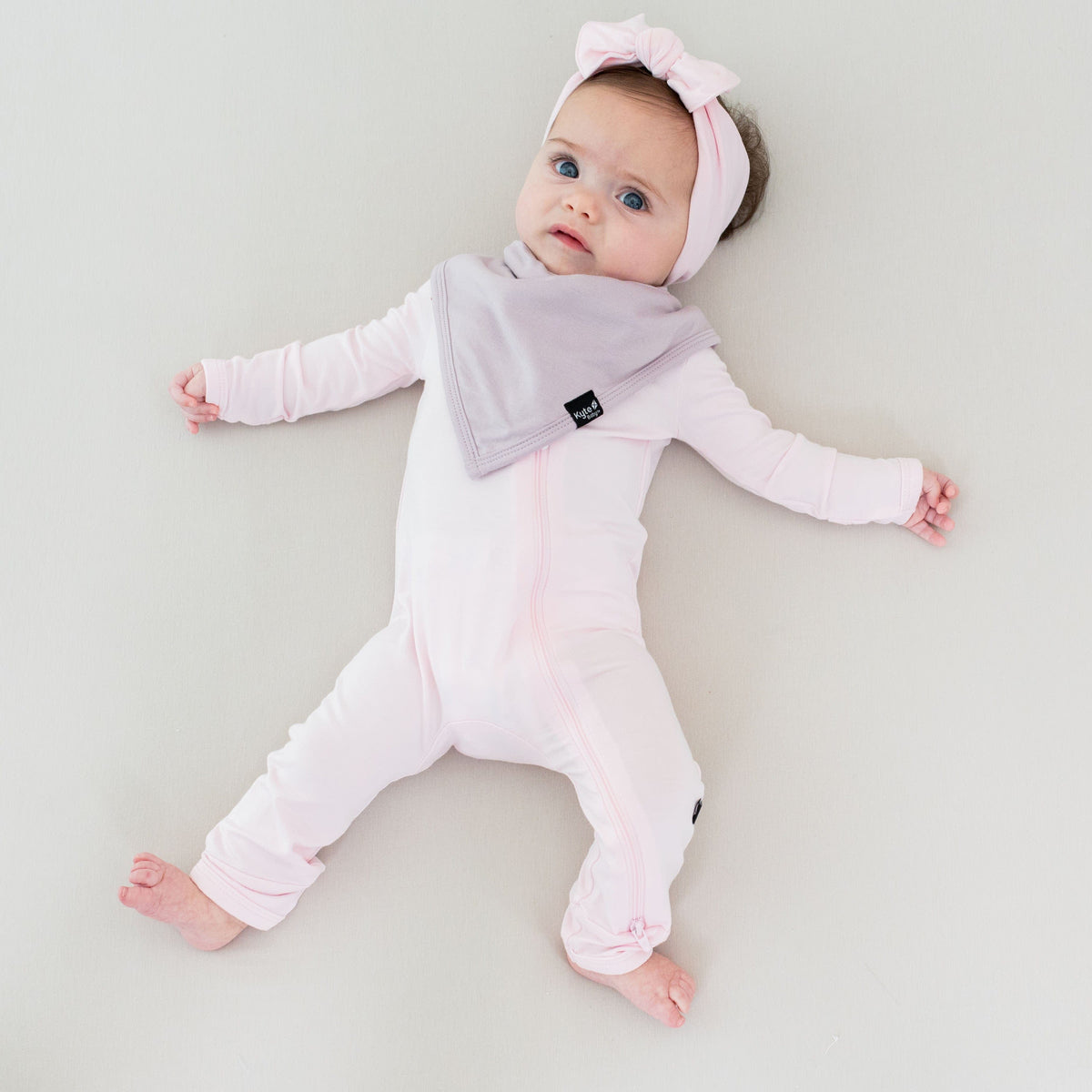 Infant wearing Kyte Baby Zippered Romper in Sakura and matching knotted headband