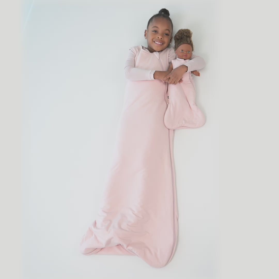 Video of a young child model wearing a Sleep Bag in Blush 1.0 holding a doll in a doll sleep bag in Blush