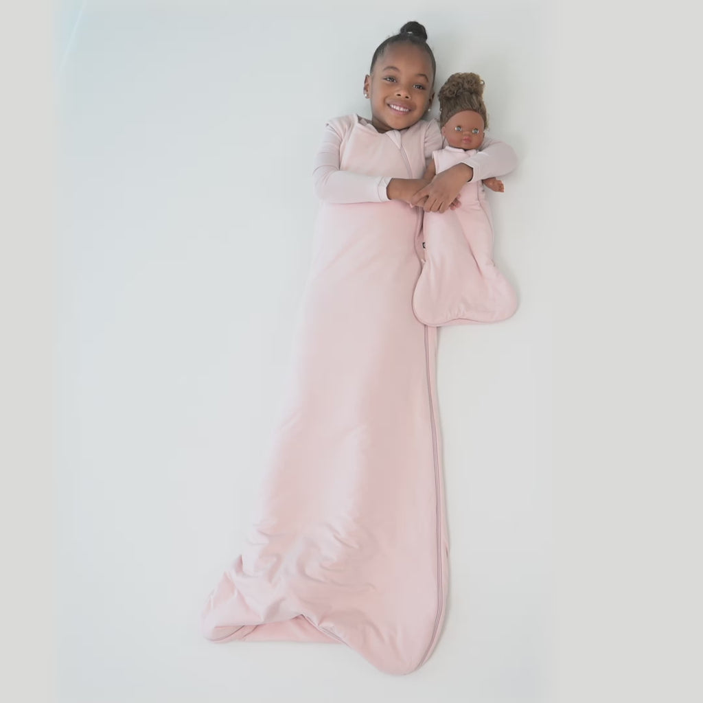 Video of a young child model wearing a Sleep Bag in Blush 1.0 holding a doll in a doll sleep bag in Blush