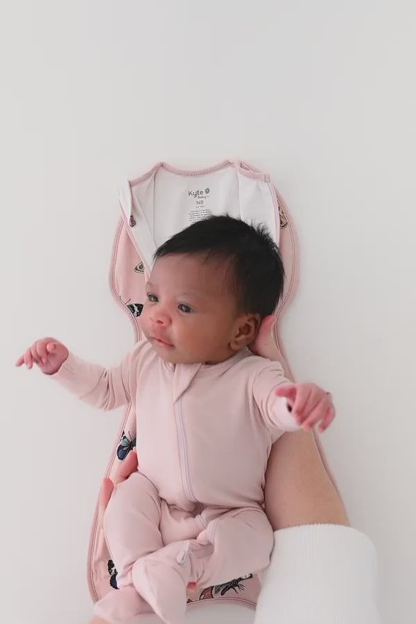 Baby being swaddled in a pink butterfly patterned swaddle bag