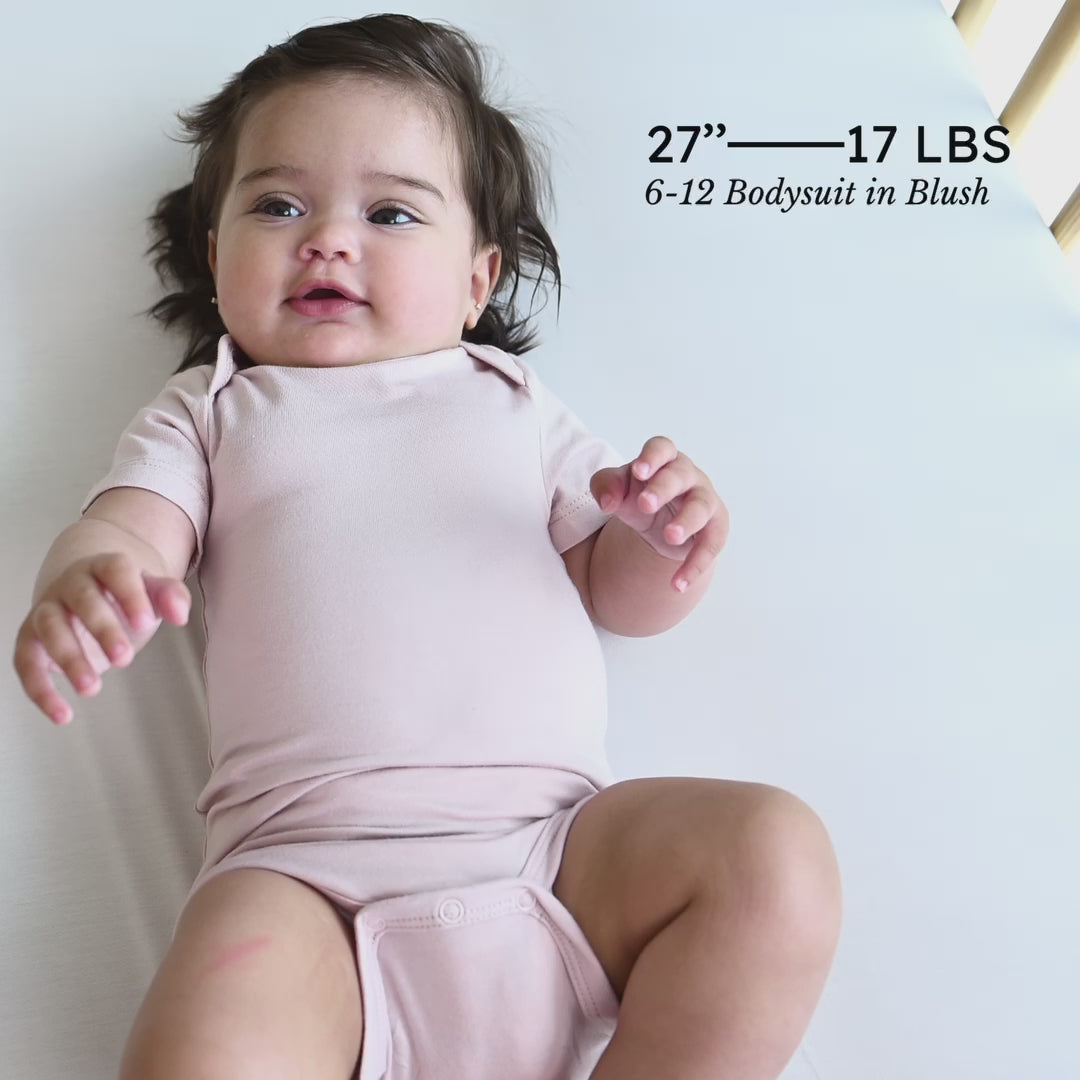 Video of baby in Kyte Baby Bodysuit in Blush with adult showing snap feature and the little one's stats
