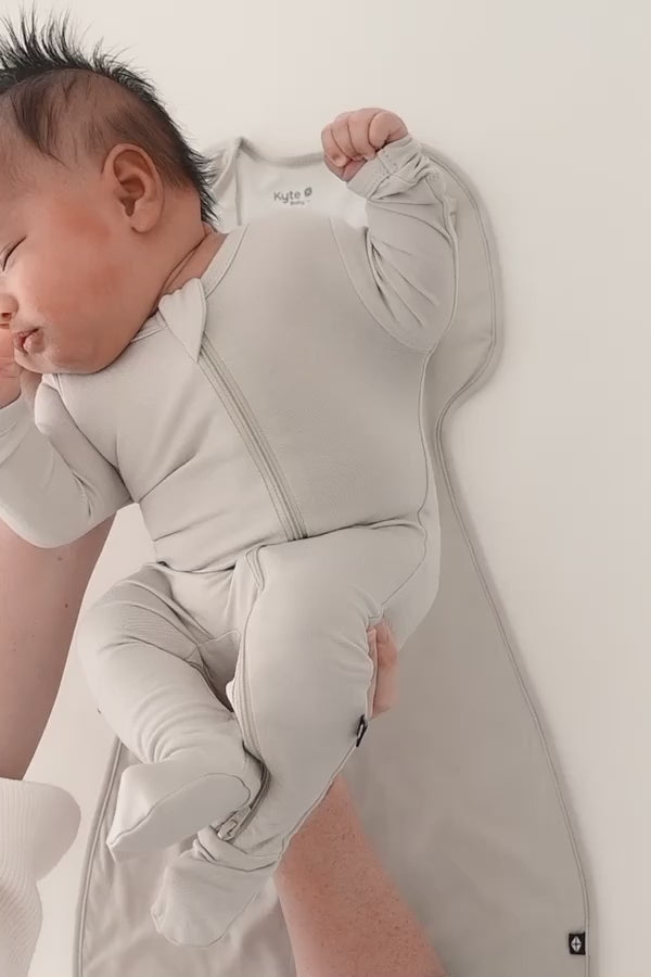 Baby being swaddled in an off white swaddle bag