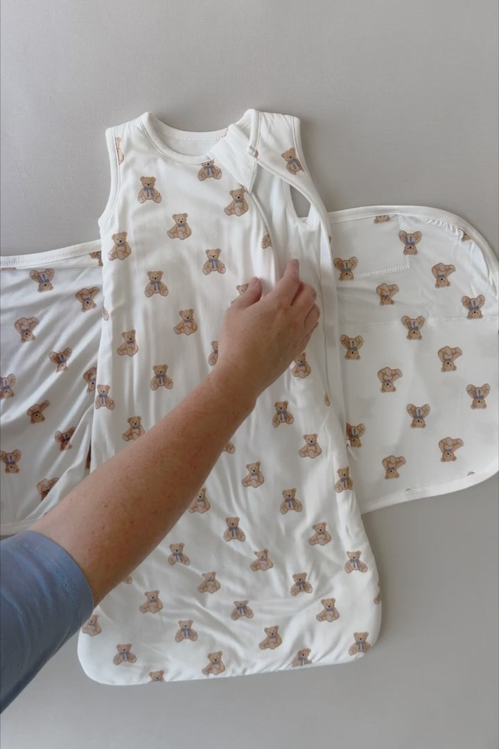 Video of a baby being swaddled in a white sleep bag swaddler with a teddy bear print 