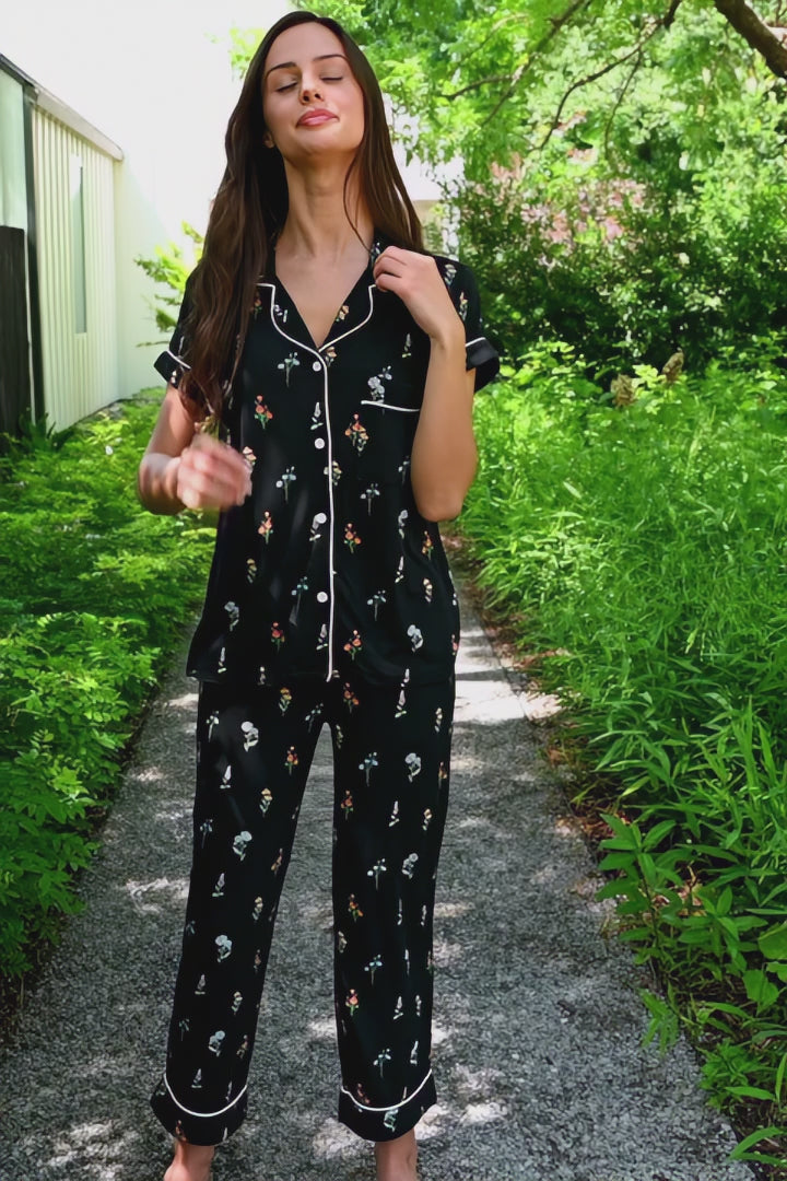 Woman modeling a black cropped short sleeve pajama set with wildflower pattern in an outdoor setting