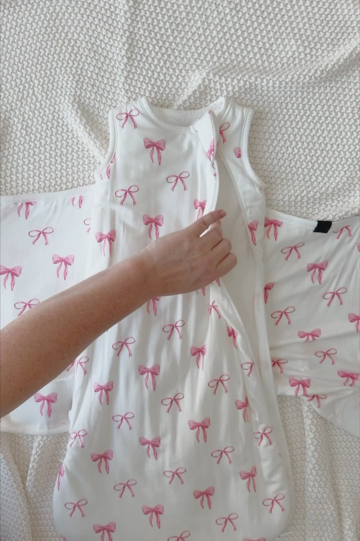 Video of a baby being swaddled in a white sleep bag swaddler with a pink bow print 