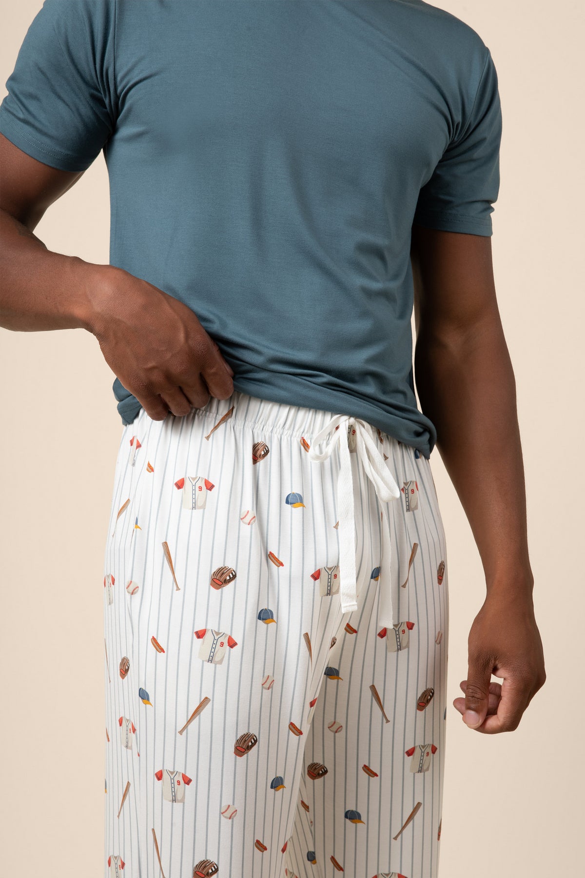 Person wearing a teal t-shirt and baseball patterned pants on a beige background