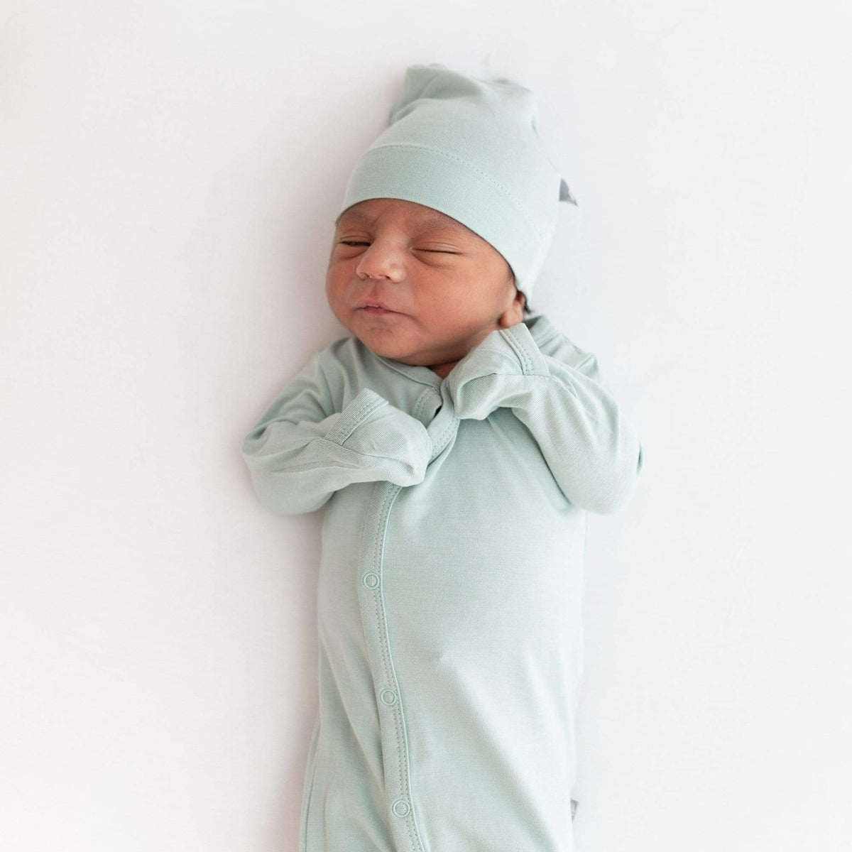 Infant sleeping in Kyte Baby bamboo Knotted Cap in Sage with matching footie 
