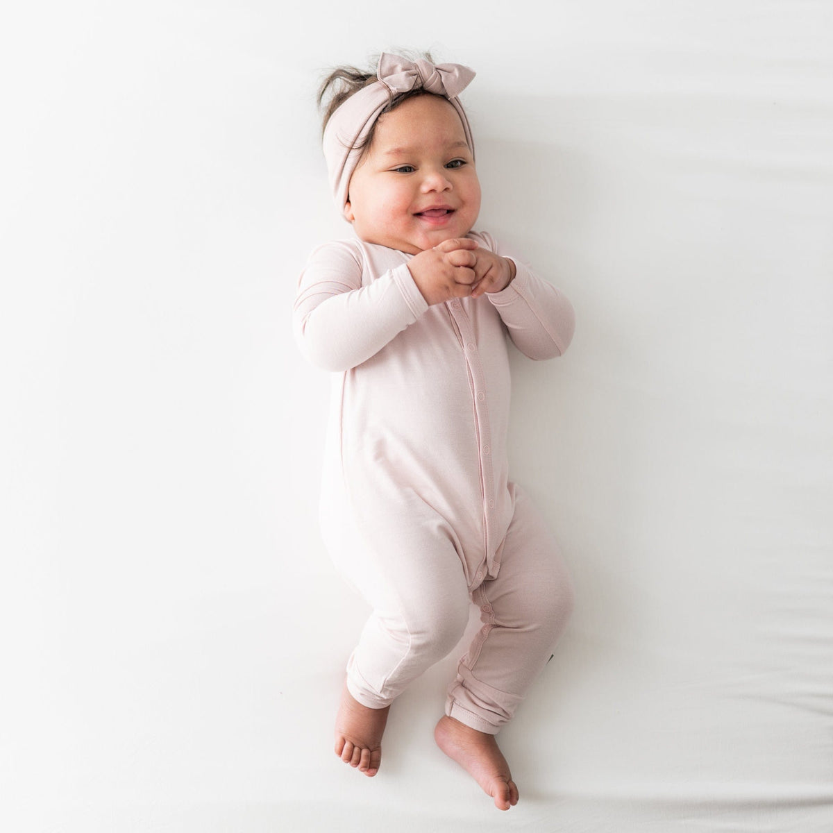 Baby laying on white surface, holding hands and wearing Romper with snaps in Blush 