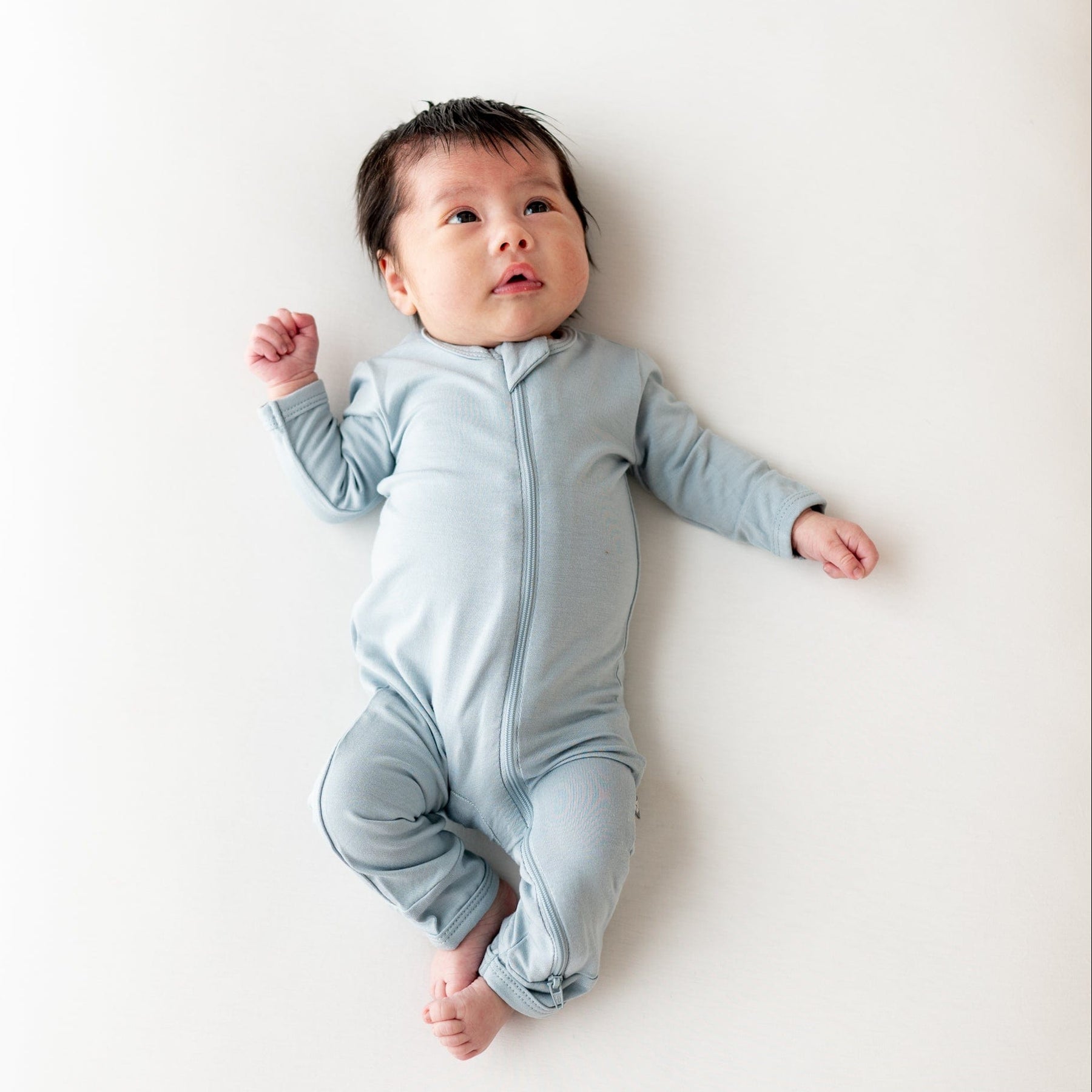 Infant laying in a crib while wearing a Zippered Romper in Fog